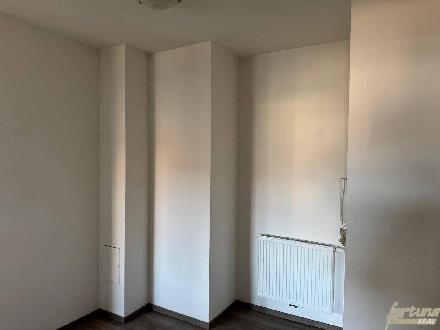 Ecke eines leeren Raumes mit weiß gestrichenen Wänden, Heizkörper und einem kleinen Kasten.