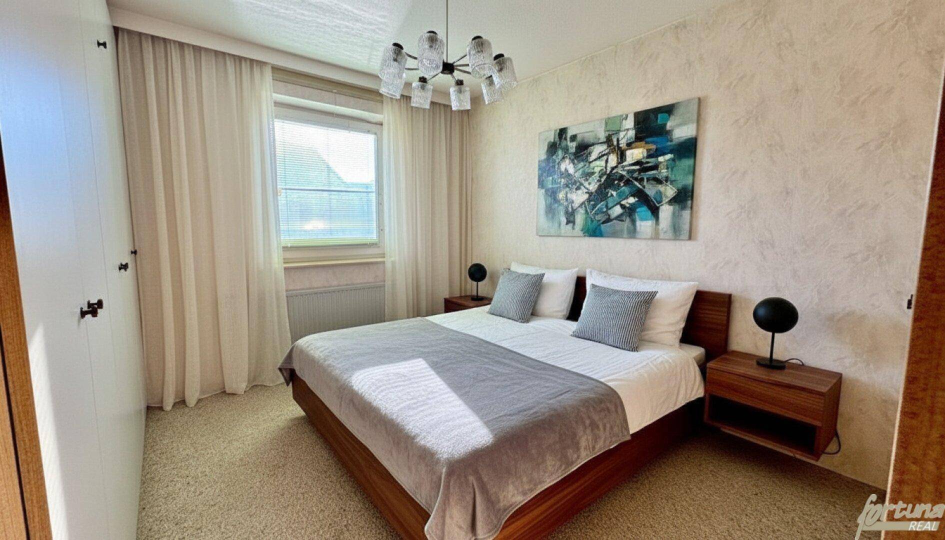 Schlafzimmer mit Doppelbett, Fenster und abstraktem Kunstwerk an der Wand.