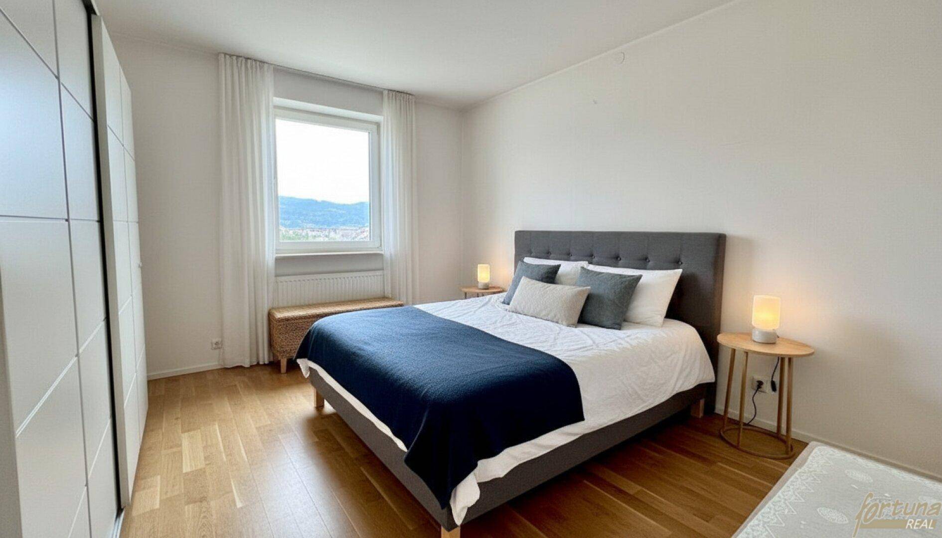 Helles Schlafzimmer mit Doppelbett, Schiebetürenschrank und Parkettboden am Fenster.