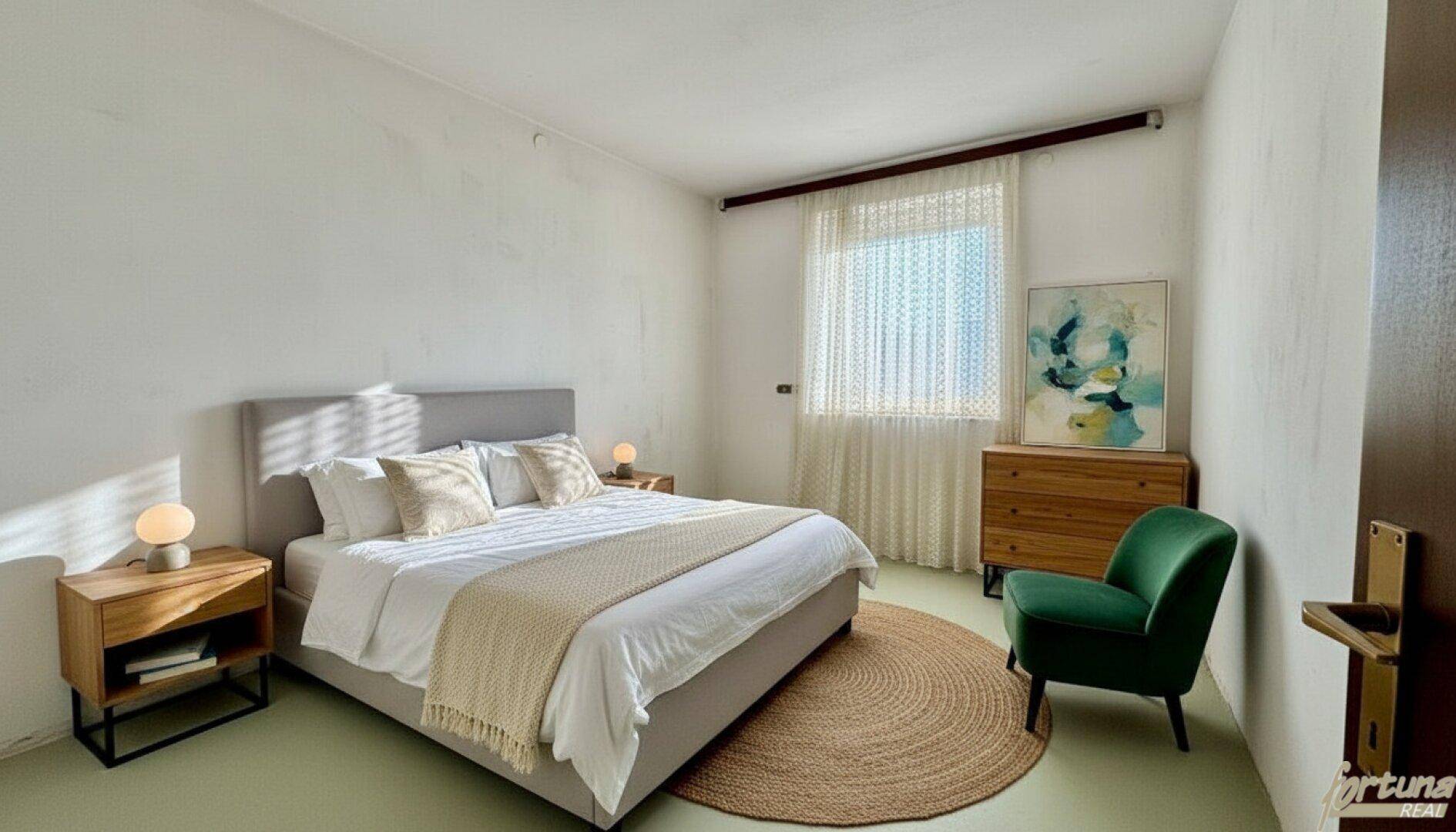 Helles Schlafzimmer mit modernem Bett, Holzakzenten und einem grünen Sessel am Fenster.