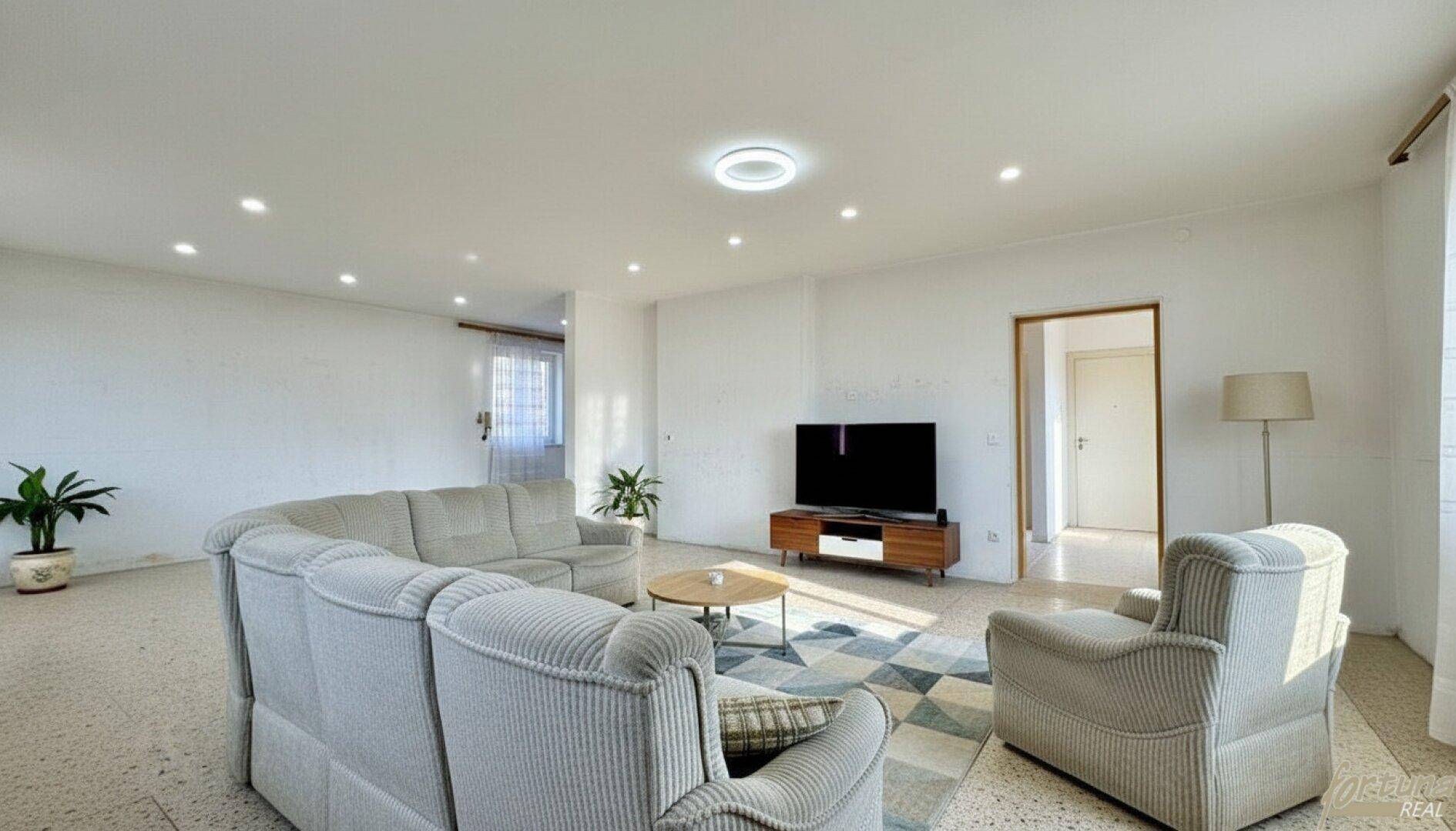 Heller Wohnbereich mit großem U-förmigem Sofa, Teppich und Terrazzoboden.