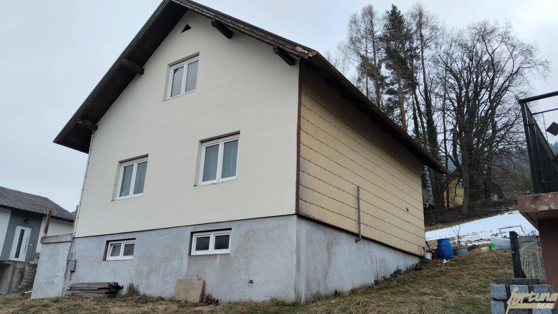 Seitenansicht eines Hauses mit beiger Fassade und Satteldach auf einem Hanggrundstück.