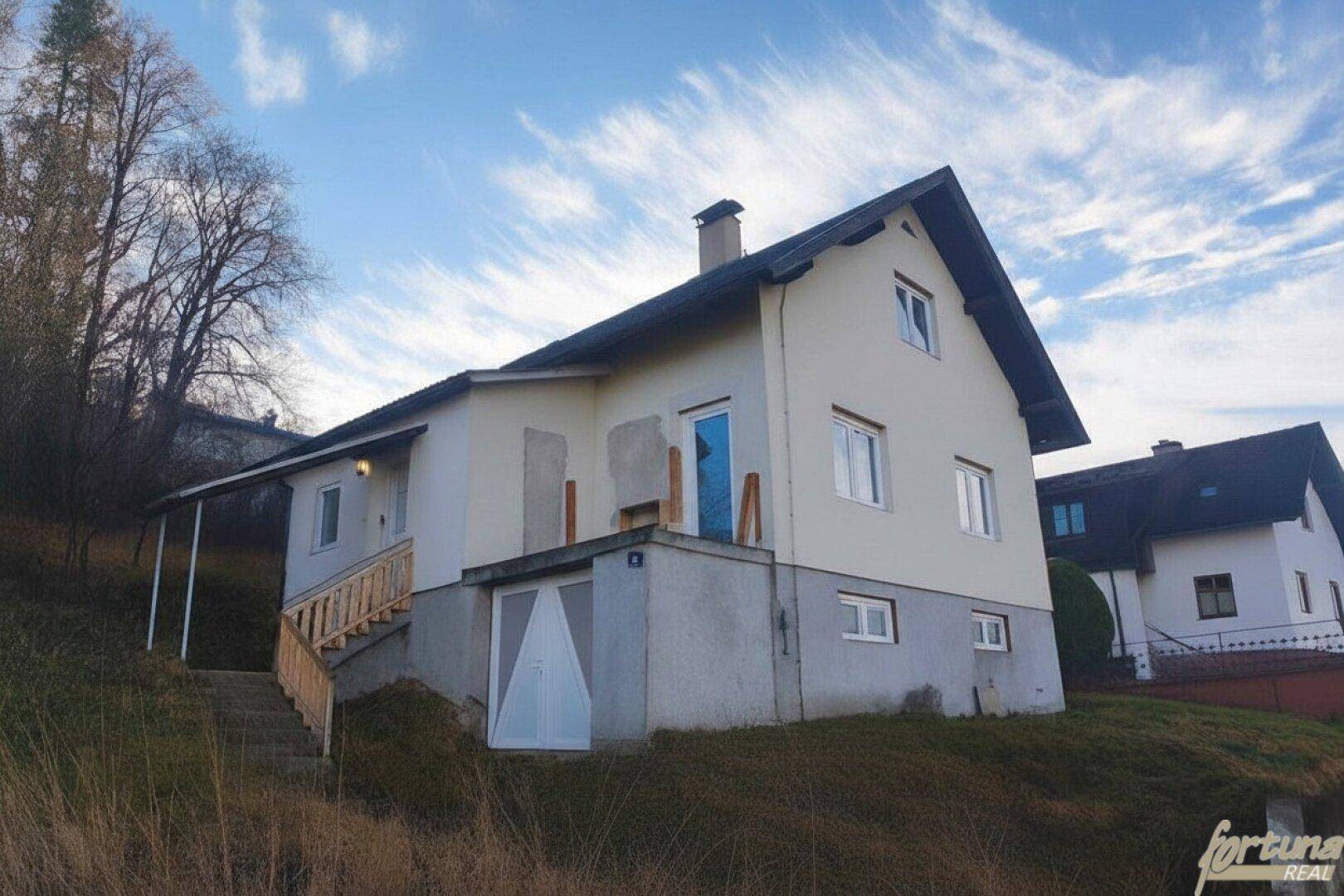 Haus auf einem Hanggrundstück mit Außentreppe und Satteldach unter blauem Himmel.