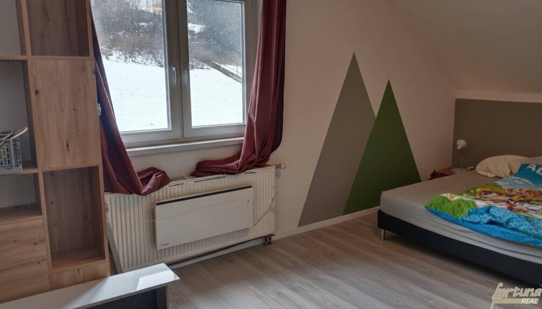 Gemütliches Schlafzimmer mit Holzboden, Fensterblick und dekorativen Wandmalereien.