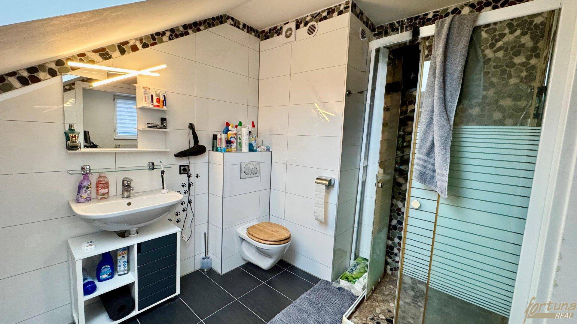 Modernes Badezimmer im Dachgeschoss mit Dusche, WC und Waschbecken.