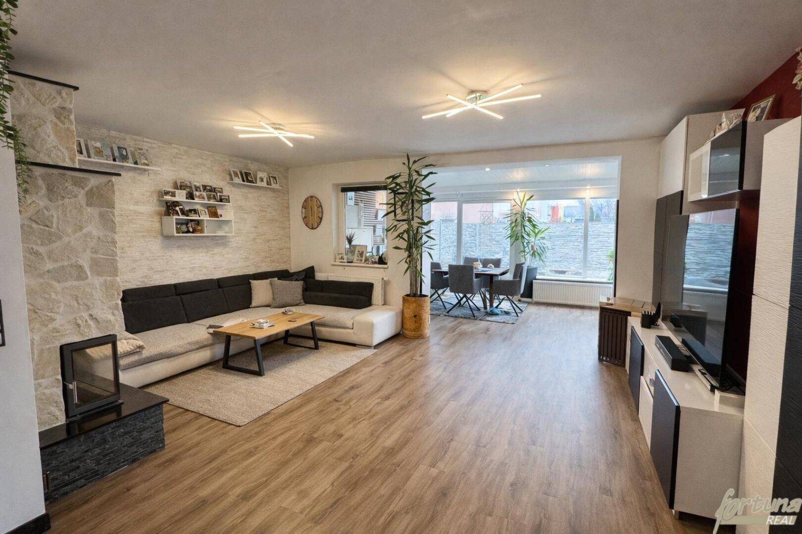 Gemütliches Wohnzimmer mit Steinwand, modernem Sofa und Blick in den Wintergarten.