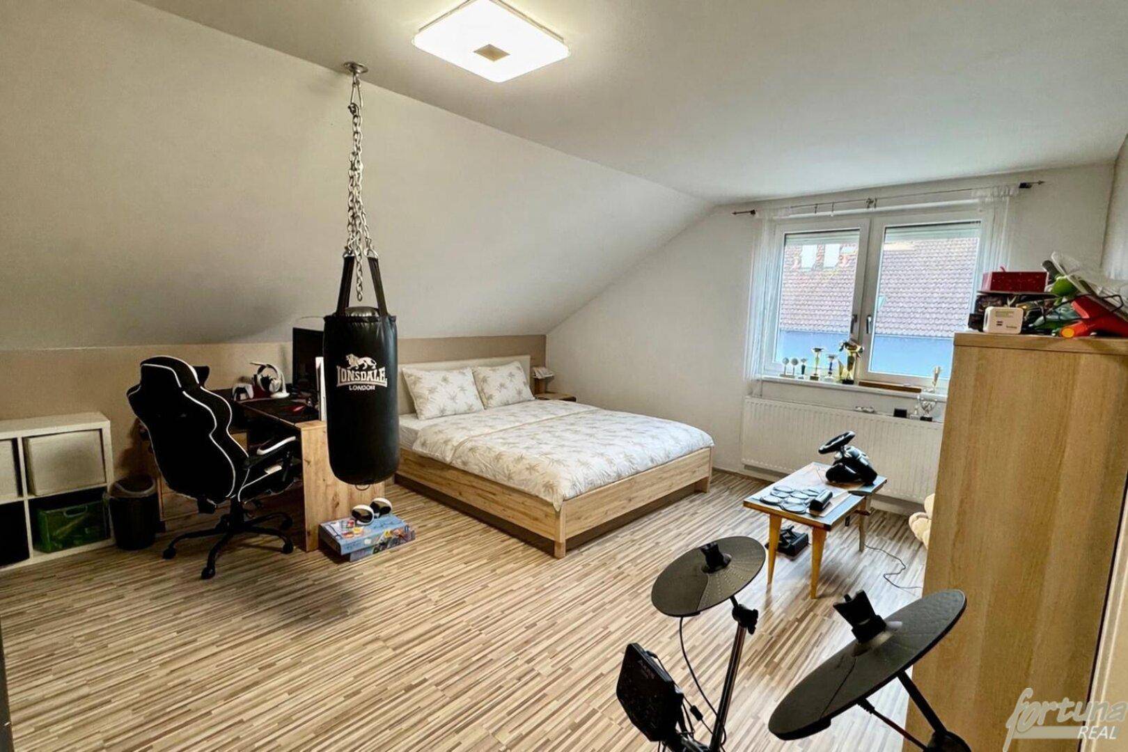 Geräumiges Schlafzimmer im Dachgeschoss mit Schreibtisch, Bett und Sportausrüstung.