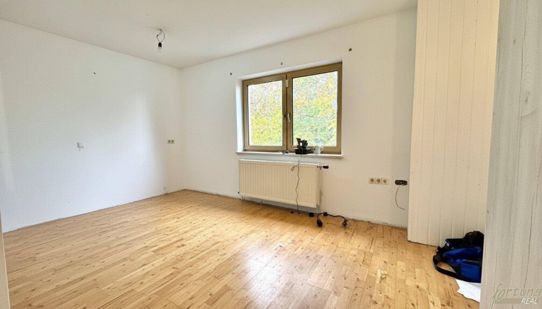 Helles, unmöbliertes Zimmer mit Holzboden und großem Fenster.