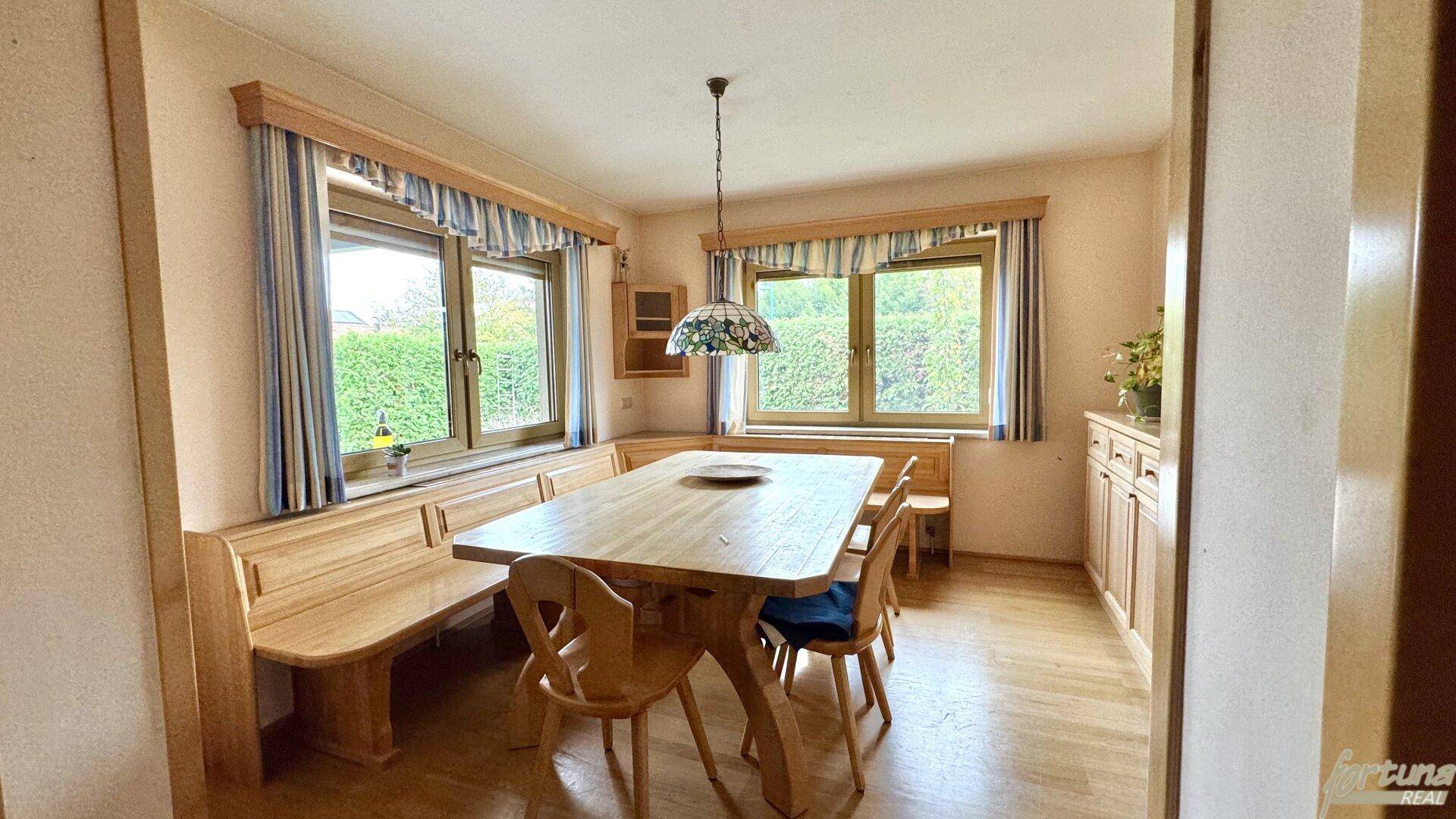 Gemütlicher Essbereich mit Holztisch, Eckbank und Blick in den grünen Garten.