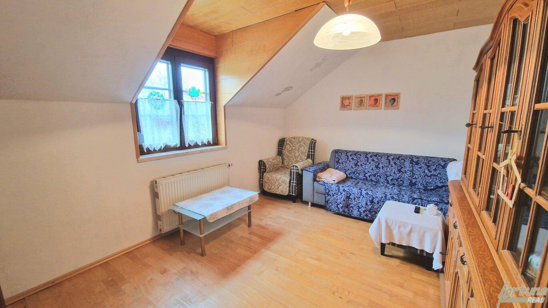 Gemütliches Wohnzimmer im Dachgeschoss mit Holzboden, schrägen Decken und traditionellen Möbeln.