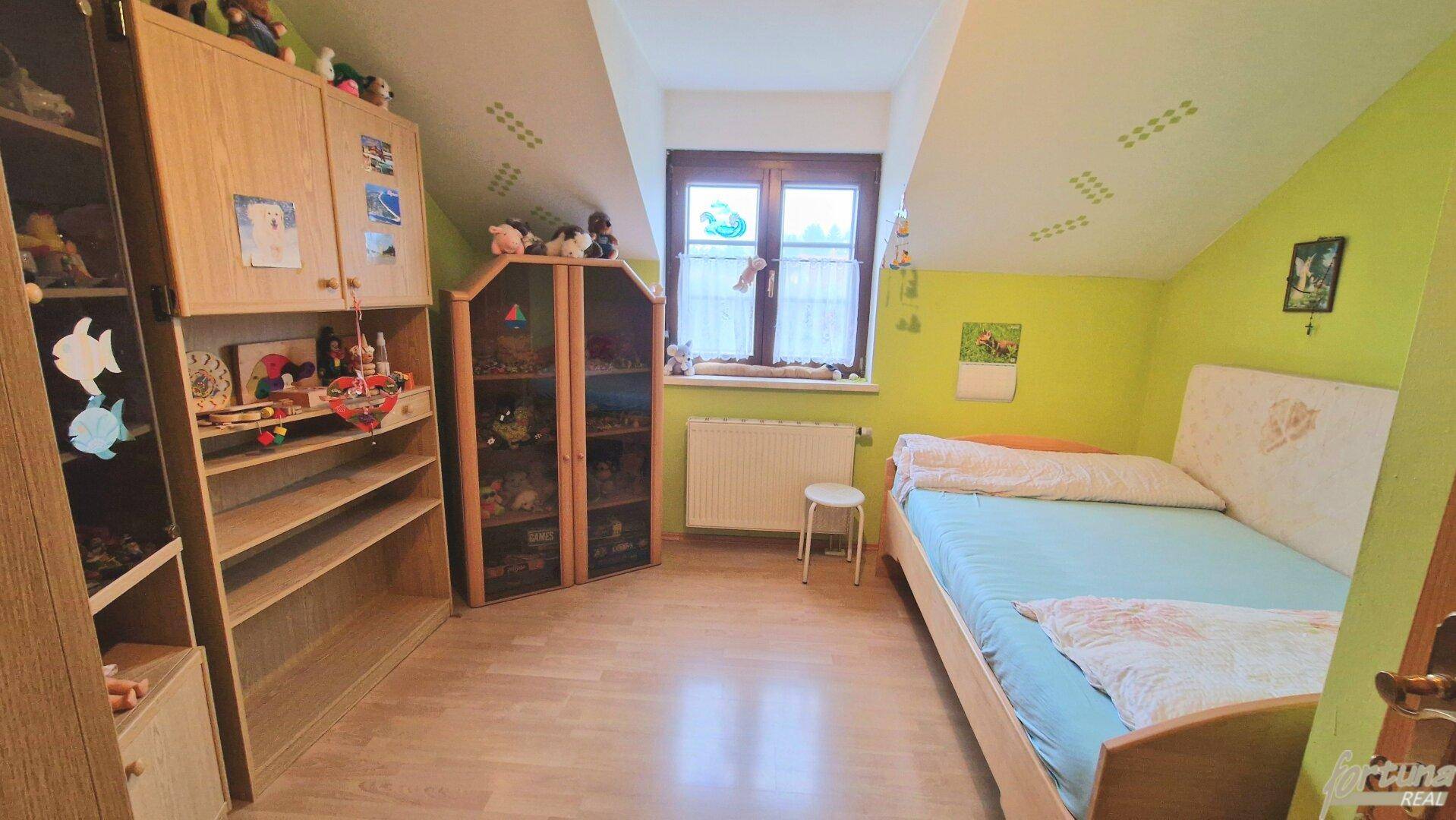 Kinderzimmer im Dachgeschoss mit grün gestrichenen Wänden, Holzboden und schrägen Decken.