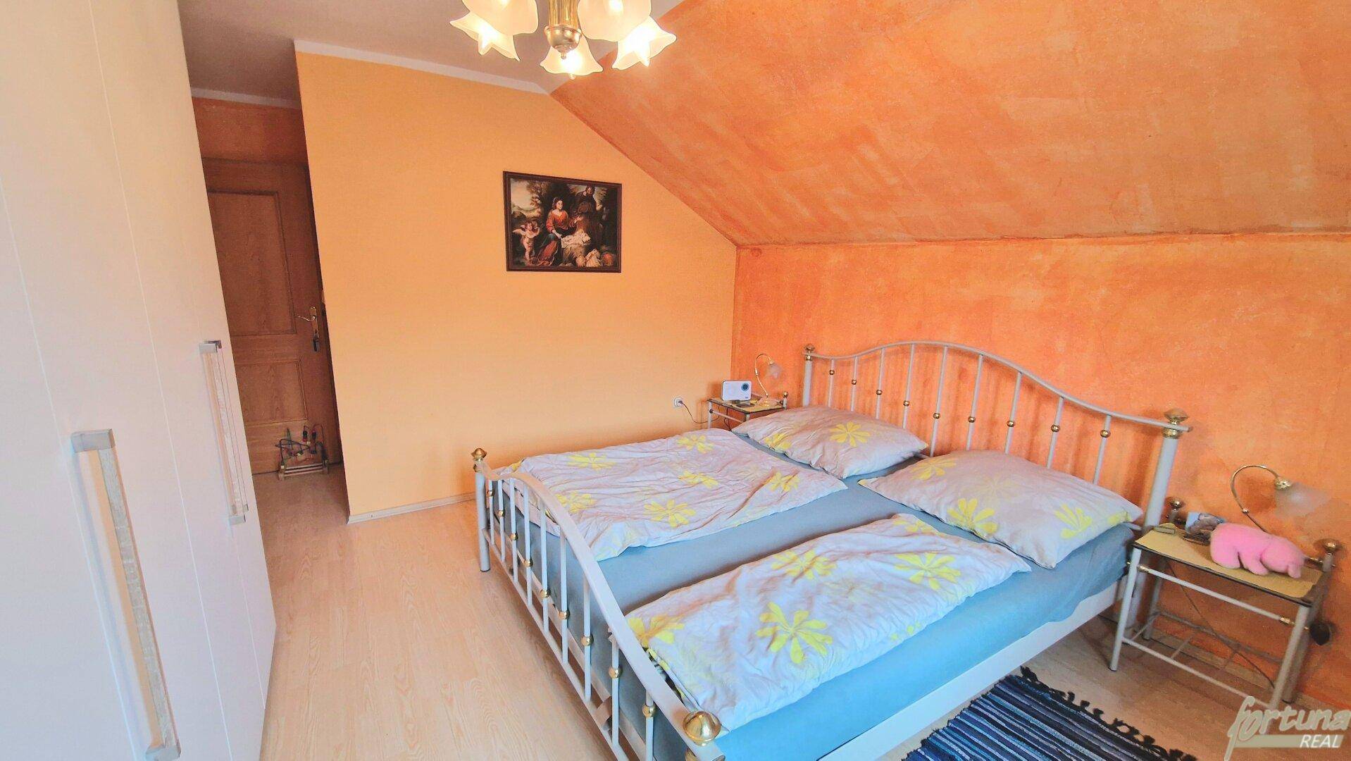 Schlafzimmer im Dachgeschoss mit orangefarbenen Wänden, Doppelbett und schrägen Decken.