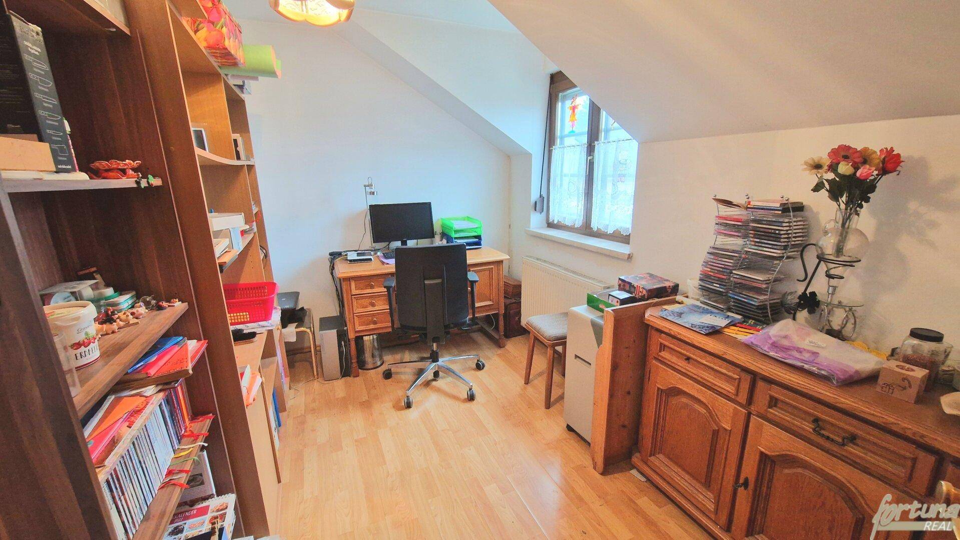 Arbeitszimmer im Dachgeschoss mit Schreibtisch, Bücherregal und Blick ins Grüne.