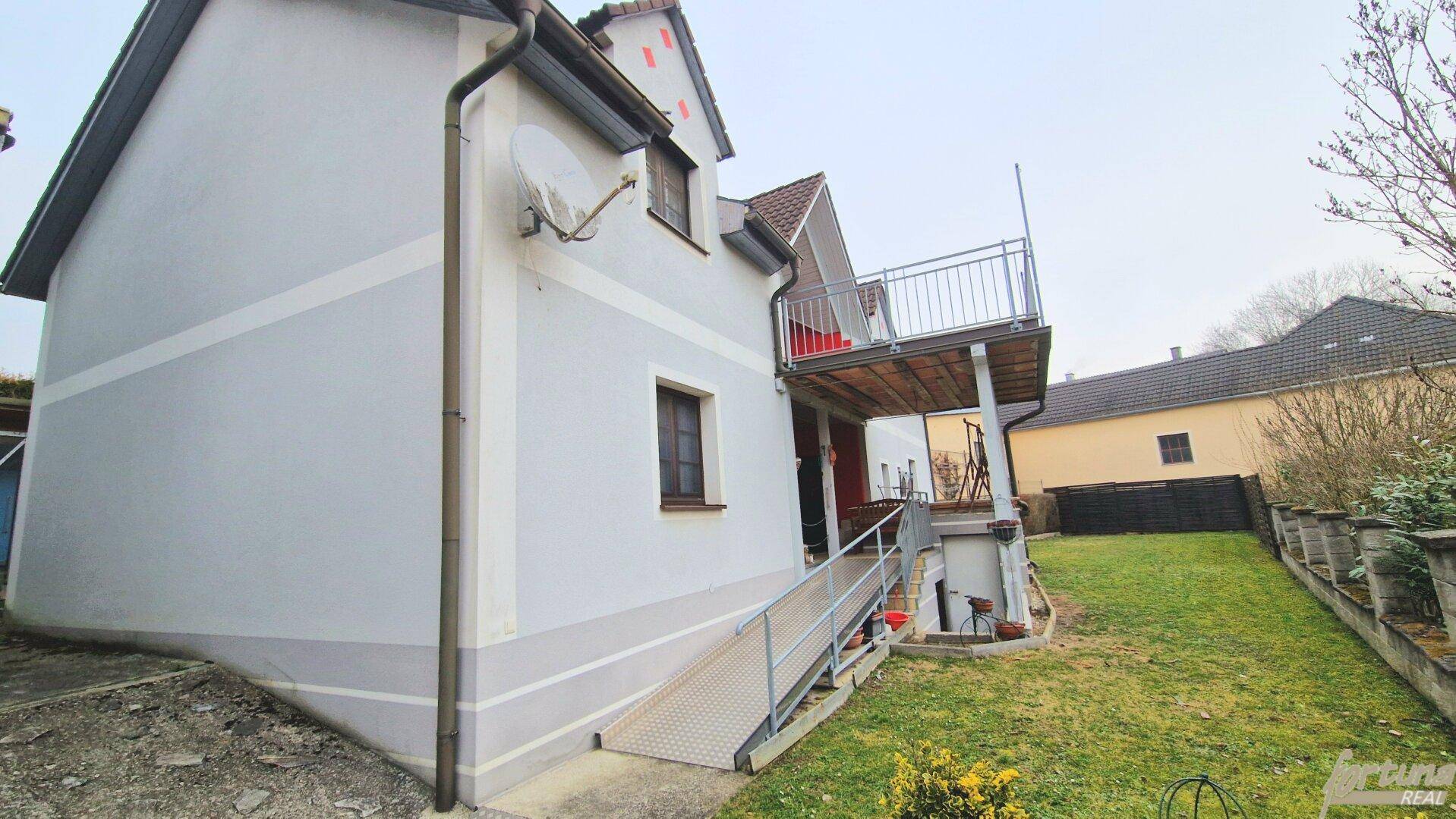 Seitenansicht des Hauses mit Rollstuhlrampe, Balkon und grünem Gartenbereich.