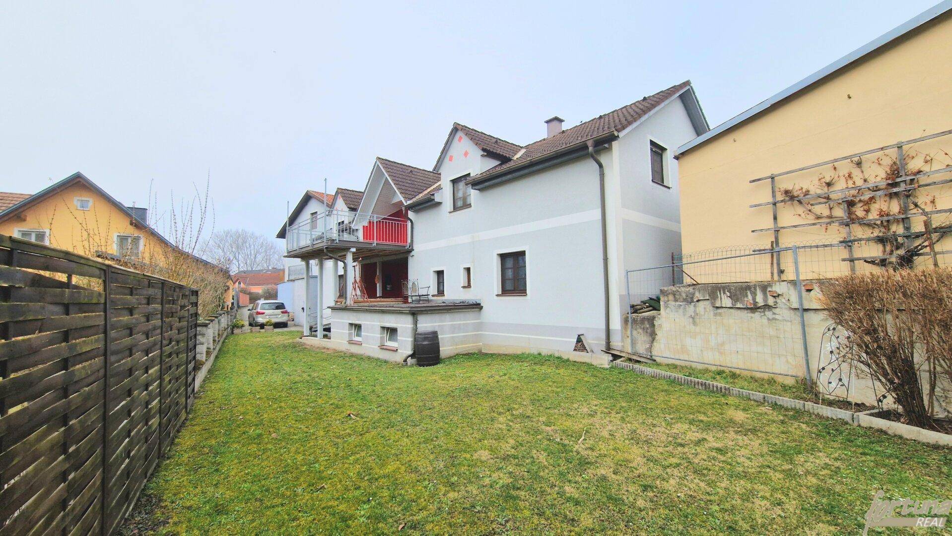 Ansicht des Hauses von der Seite mit Garten, Zaun und umliegender Bebauung.