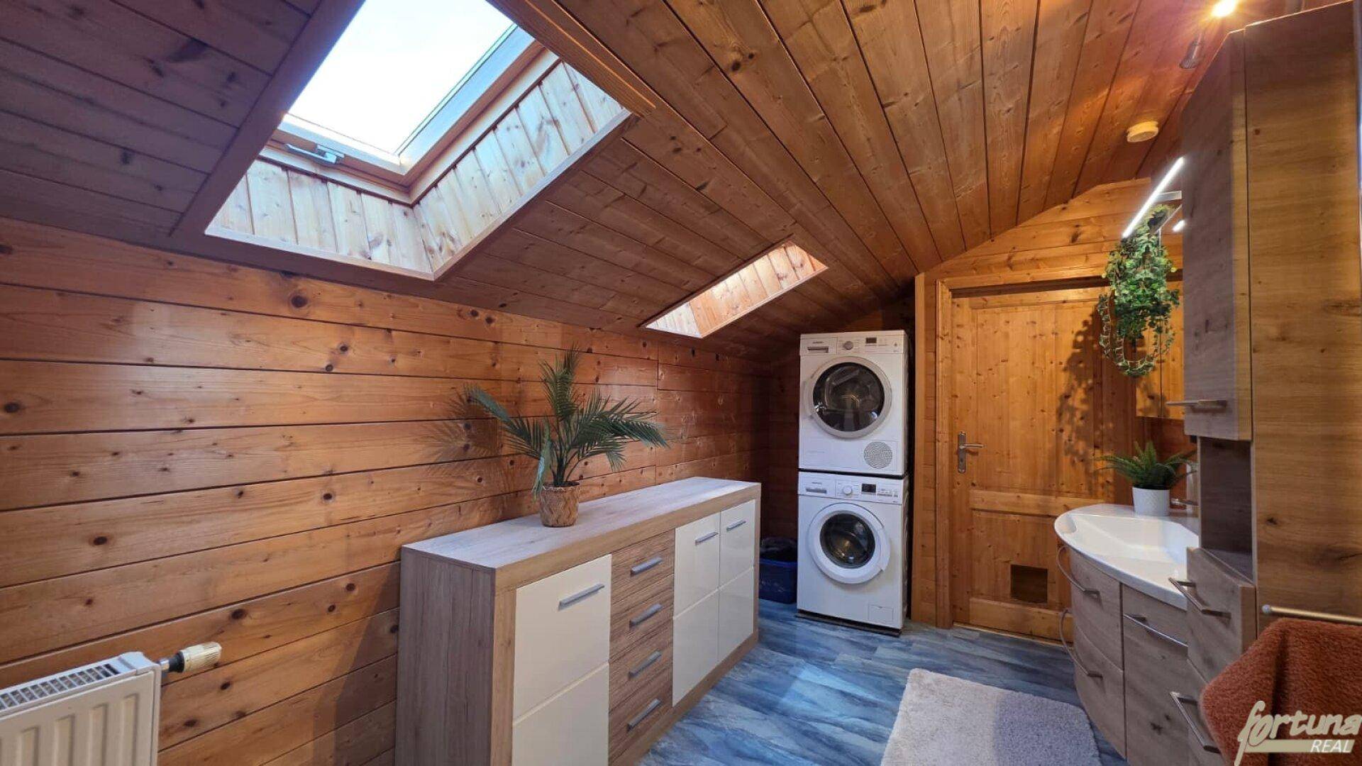 Waschküche mit Holzwänden, Dachfenstern, Waschmaschine und Trockner.