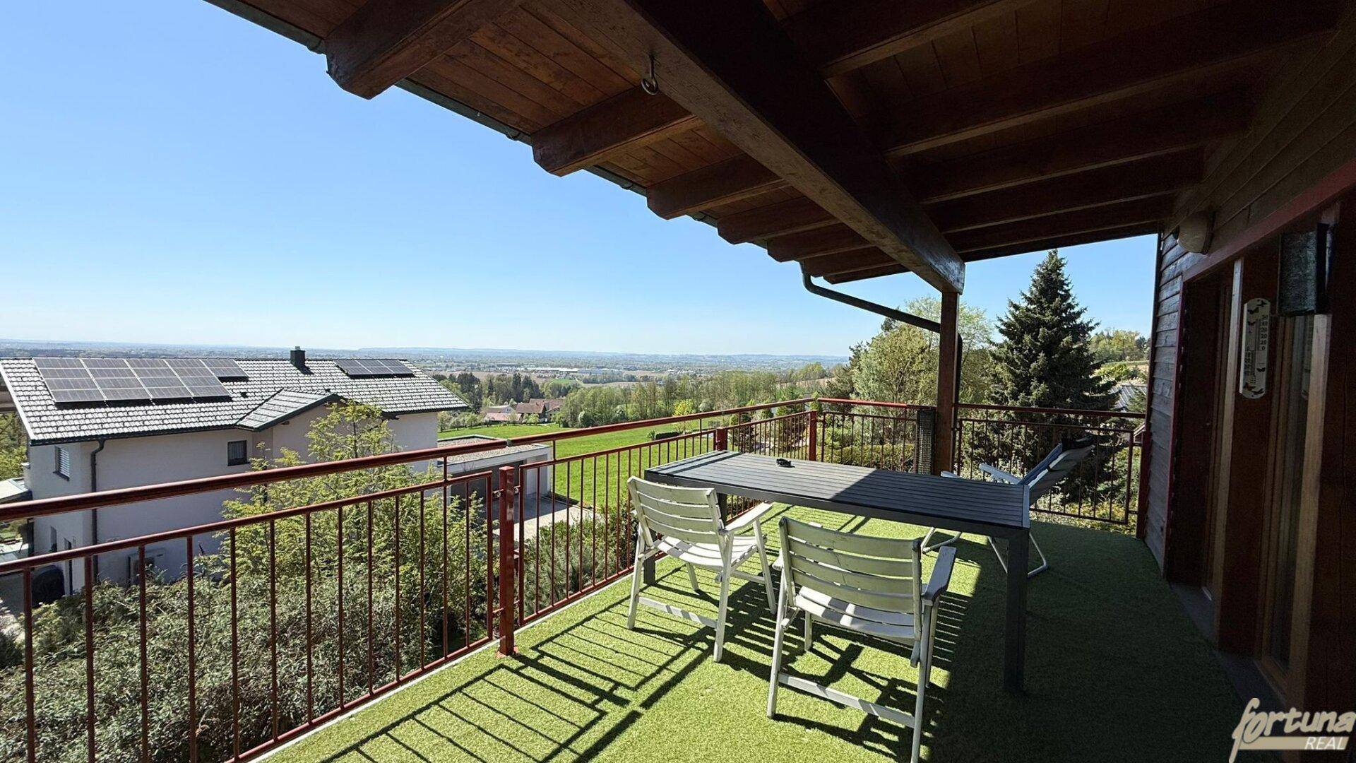 Überdachter Balkon mit Esstisch und Stühlen, bietet einen weiten Blick über die Landschaft.