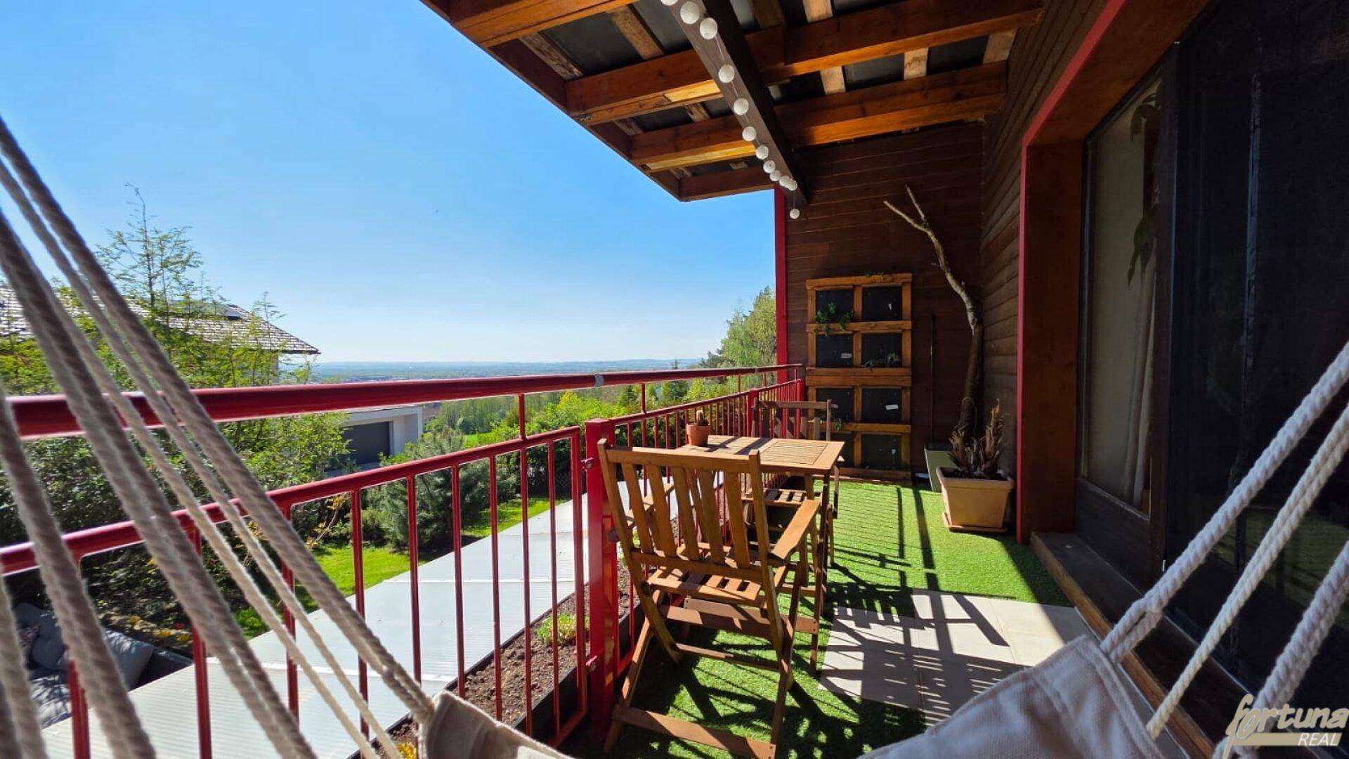 Sonniger Balkon mit Hängematte, Holzboden und rotem Geländer bietet einen weiten Blick.