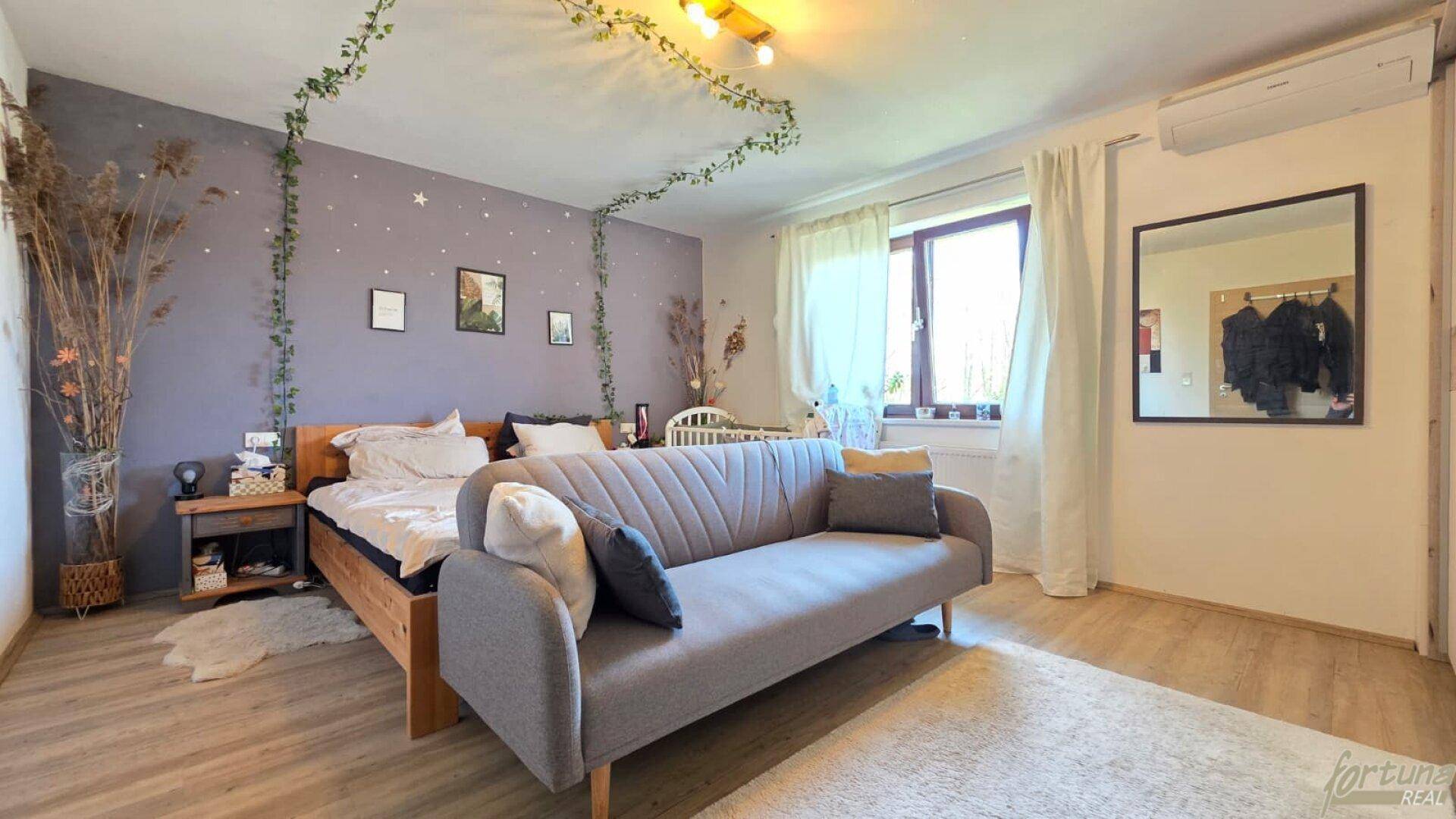Gemütliches Schlafzimmer mit Doppelbett, Sofa, Babybett und dekorativer Wandgestaltung für Entspannung.