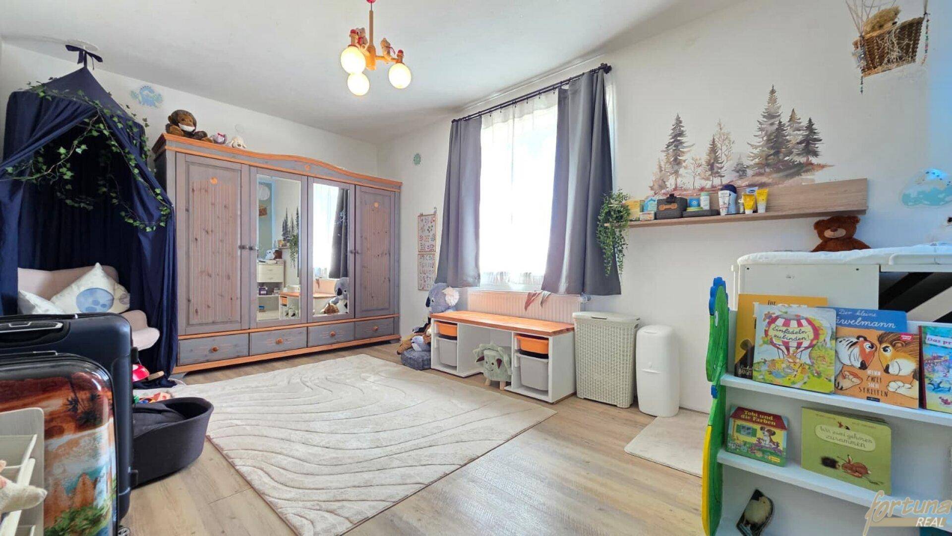 Kinderzimmer mit hellem Laminatboden, großem Kleiderschrank und verspielter Wanddekoration für Kinder.