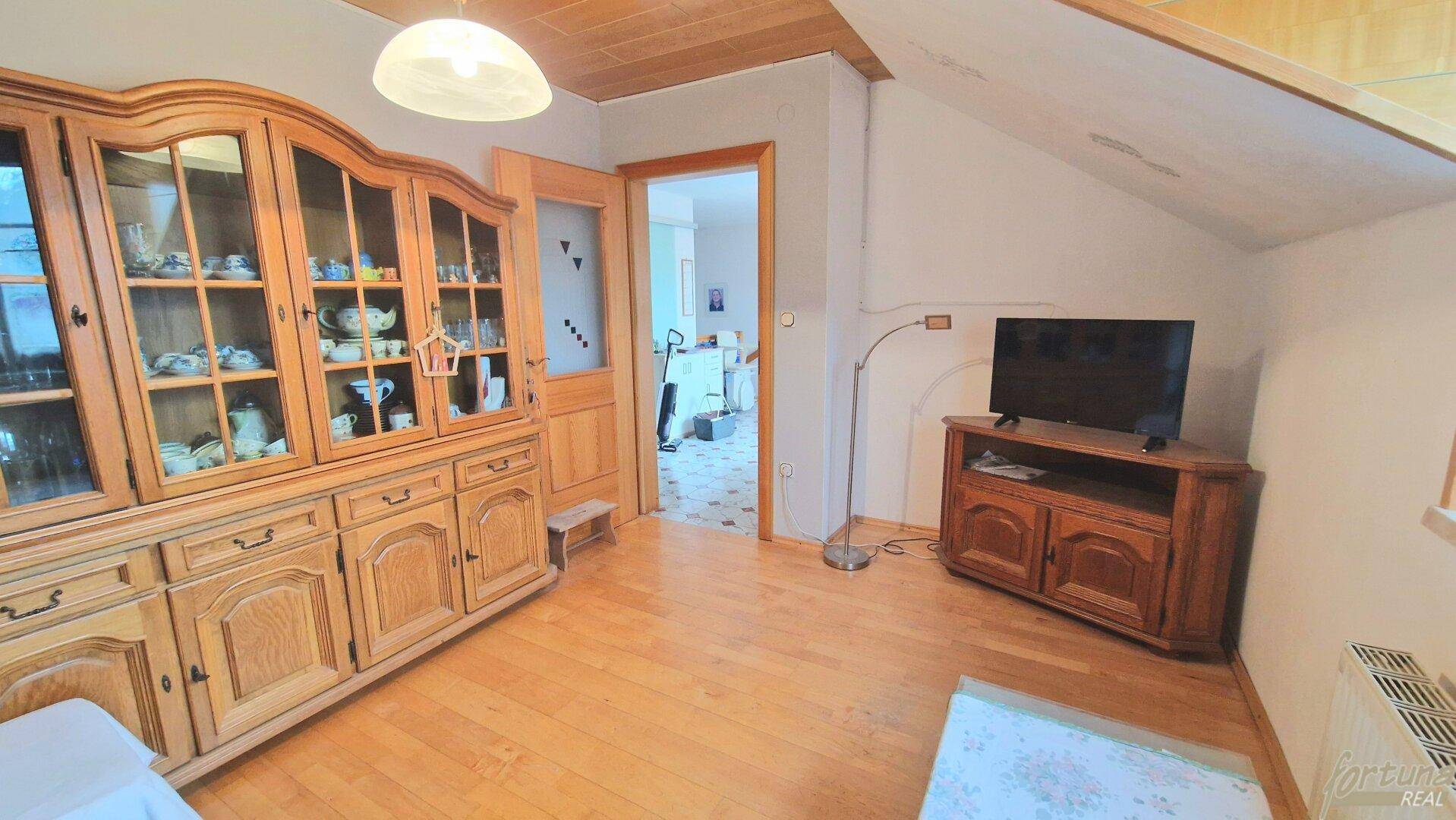 Wohnbereich im Dachgeschoss mit Holzboden, Vitrinenschrank und Dachschrägen, gemütlich eingerichtet.