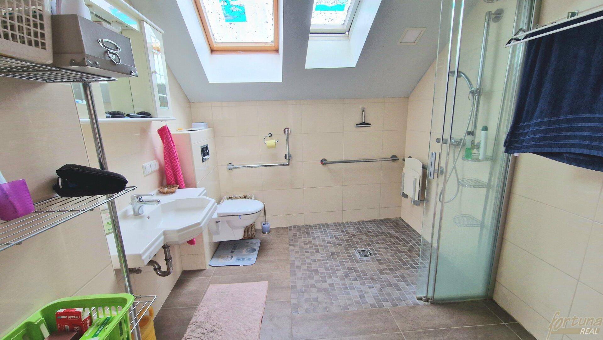 Barrierefreies Badezimmer im Dachgeschoss mit Dusche, Haltegriffen und Dachfenstern für natürliches Licht.
