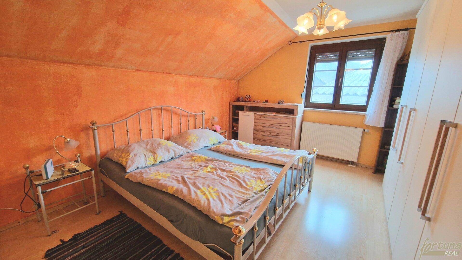 Schlafzimmer im Dachgeschoss mit orangefarbenen Wänden, Doppelbett und Dachschrägen, gemütlich gestaltet.