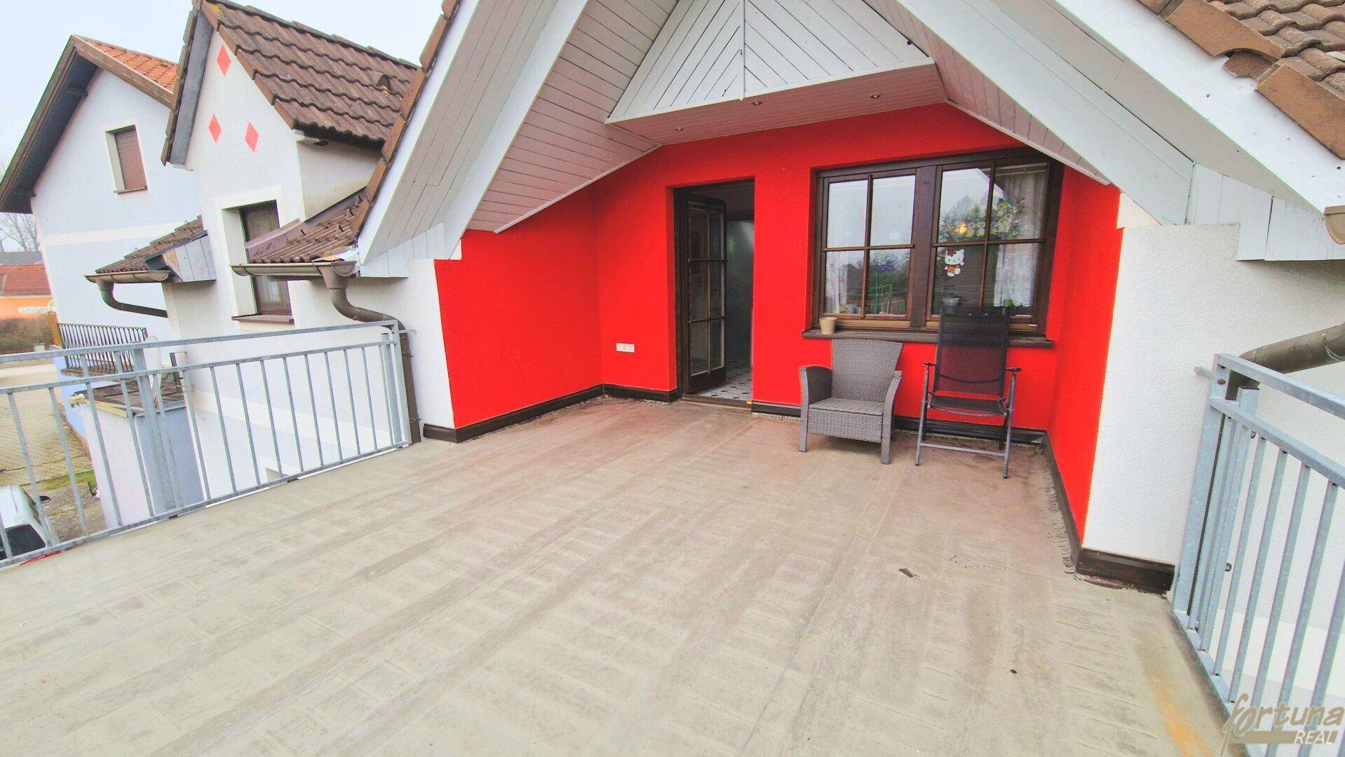 Geräumiger Balkon mit Sitzgelegenheiten und Blick auf die umliegenden Häuser und Dächer.