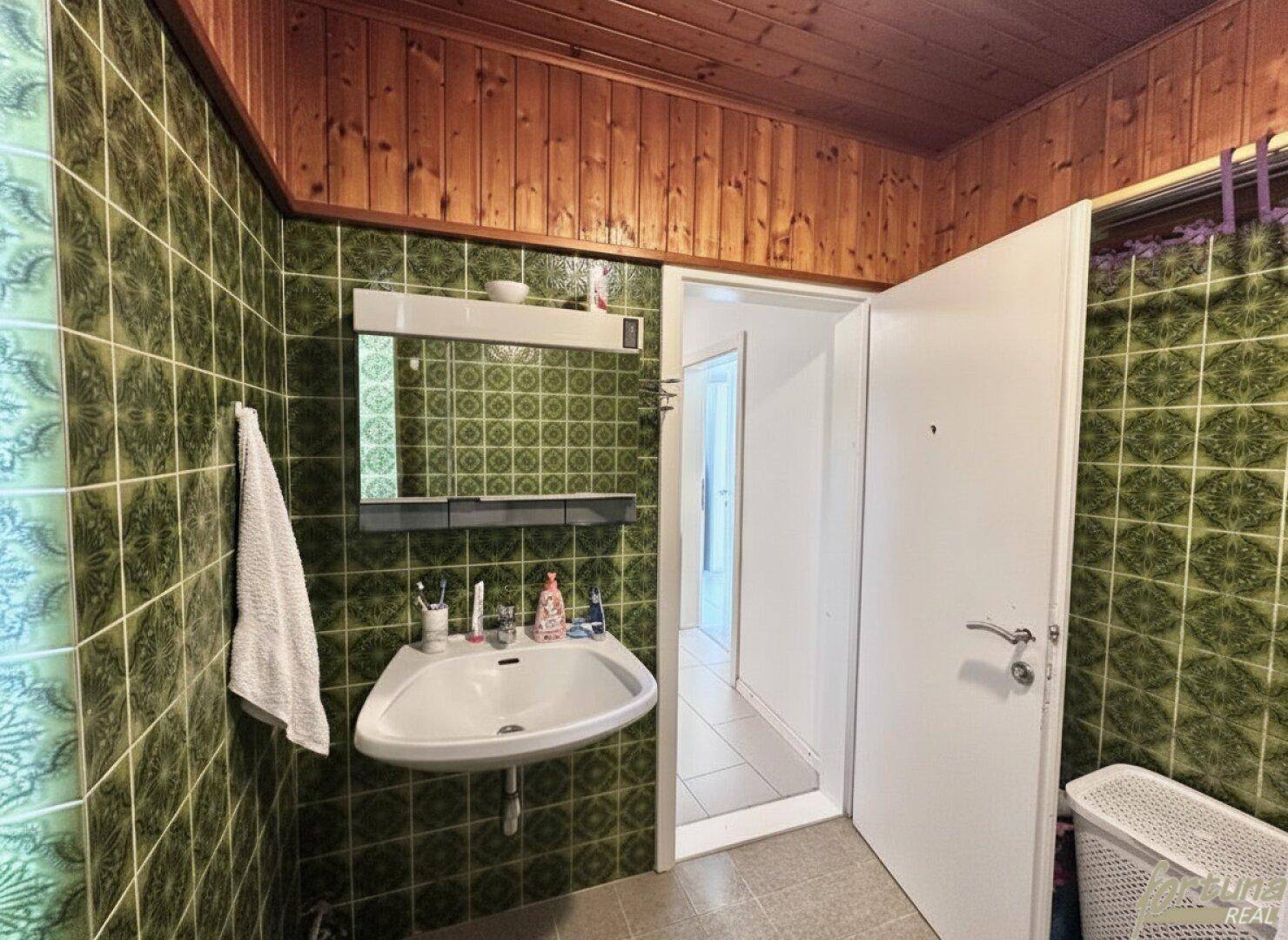 Badezimmer mit auffälligen grünen Fliesen an den Wänden und einer Holzverkleidung an der Decke.