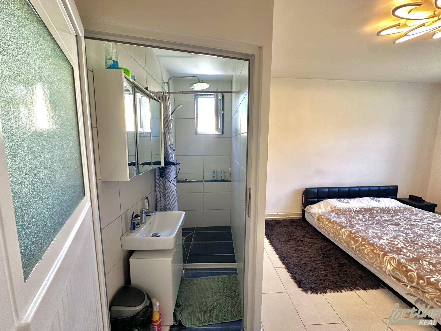 Schlafzimmer mit Bett und direktem Zugang zu einem kompakten Badezimmer mit Dusche und Waschbecken.
