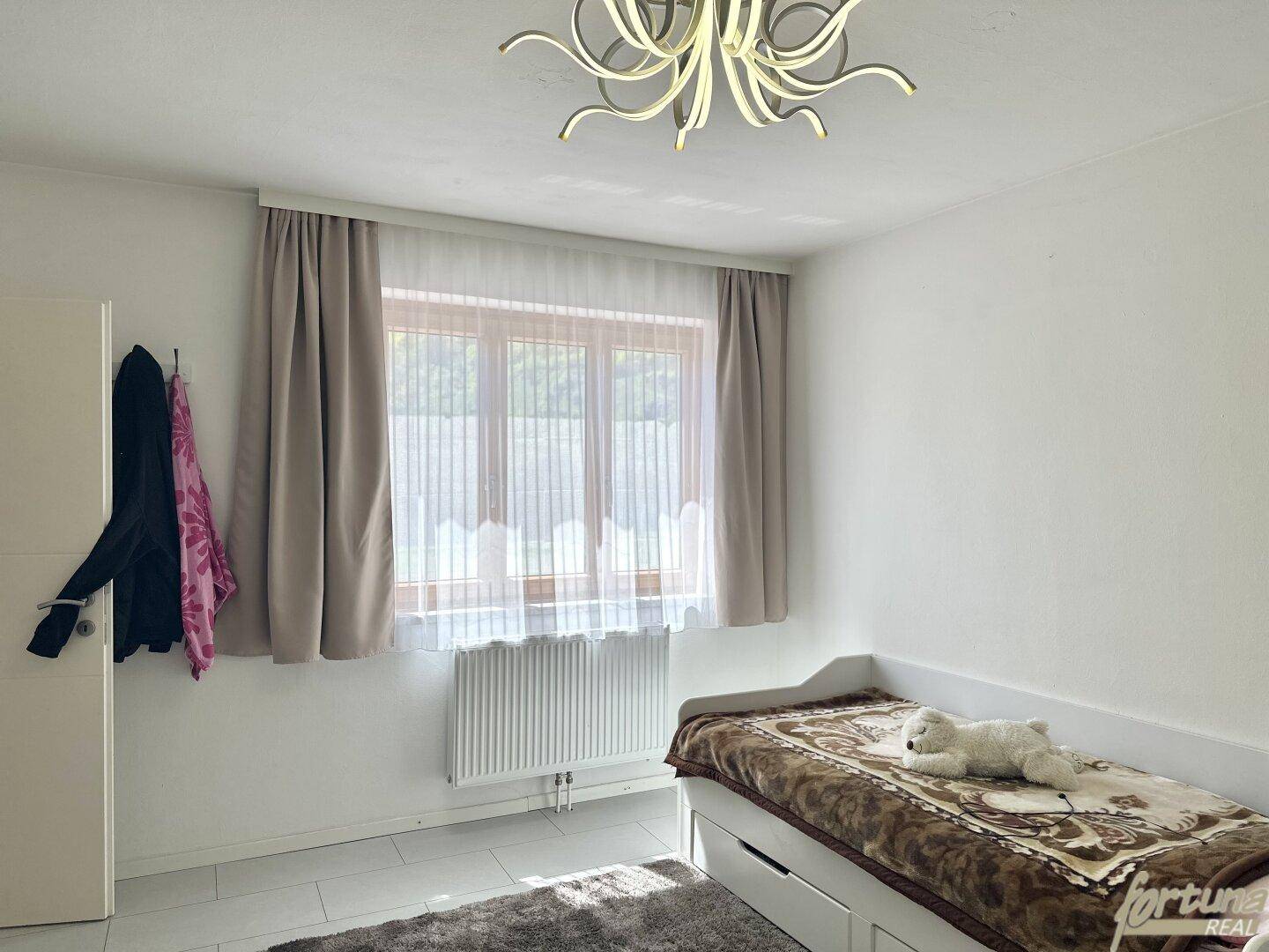 Helles Schlafzimmer mit Einzelbett, Teppich und einem Fenster, das viel Tageslicht hereinlässt.