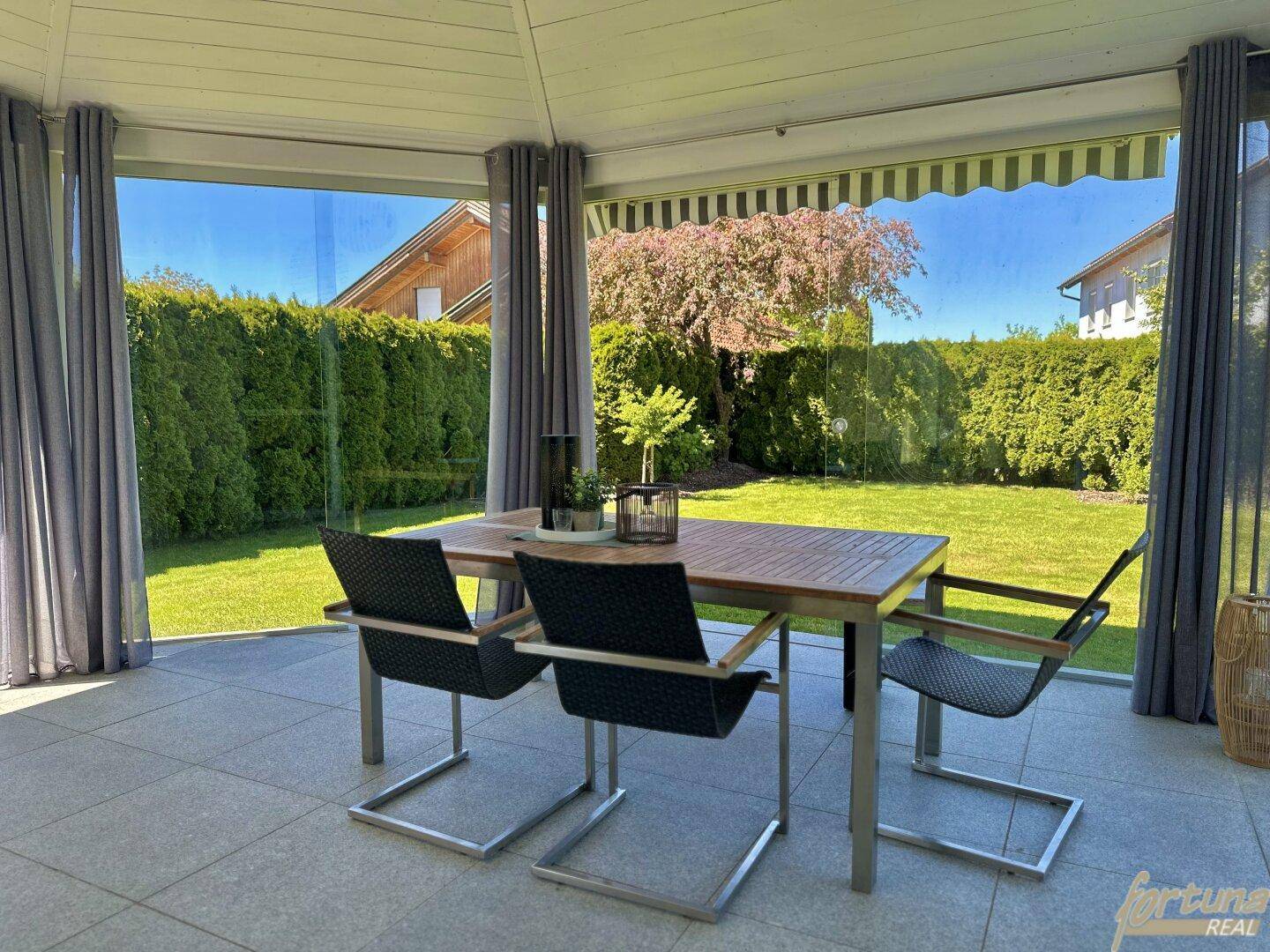 Verglaste Terrasse mit Esstisch und Stühlen, ideal für Mahlzeiten im Freien mit Gartenblick.