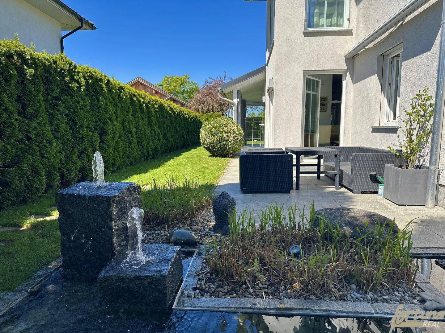 Gepflegter Gartenbereich mit Wasserspiel, Teich und einer gemütlichen Sitzgelegenheit im Freien.