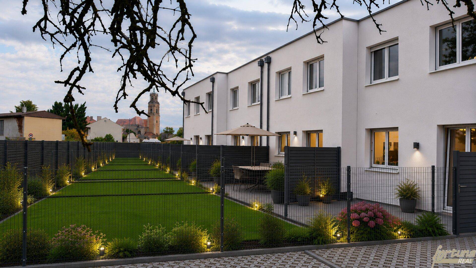 Moderne Reihenhäuser mit privaten Terrassen und gepflegten Gärten am Abend.