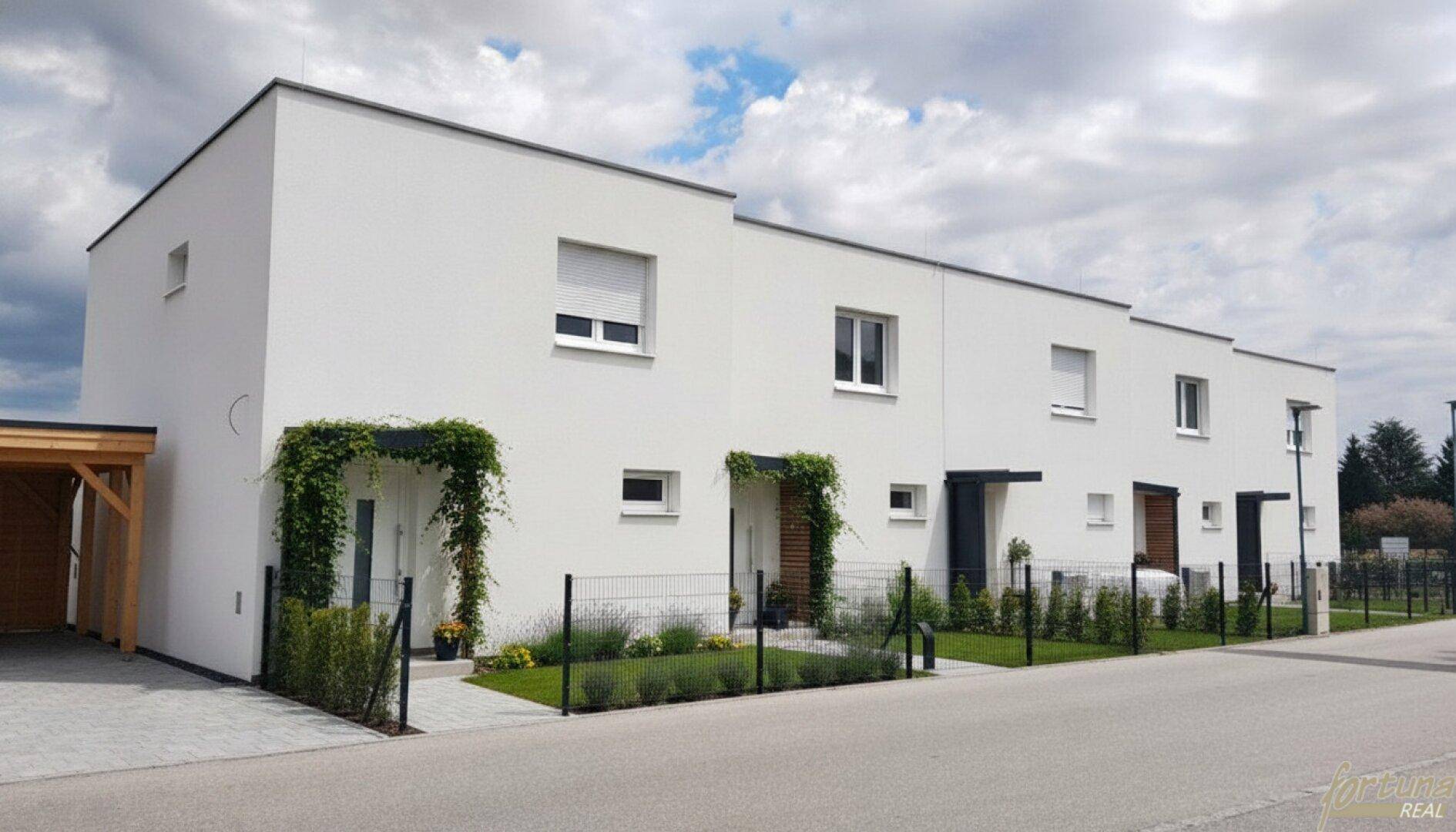 Reihenhäuser mit moderner Architektur, weißen Fassaden und begrünten Eingangsbereichen.