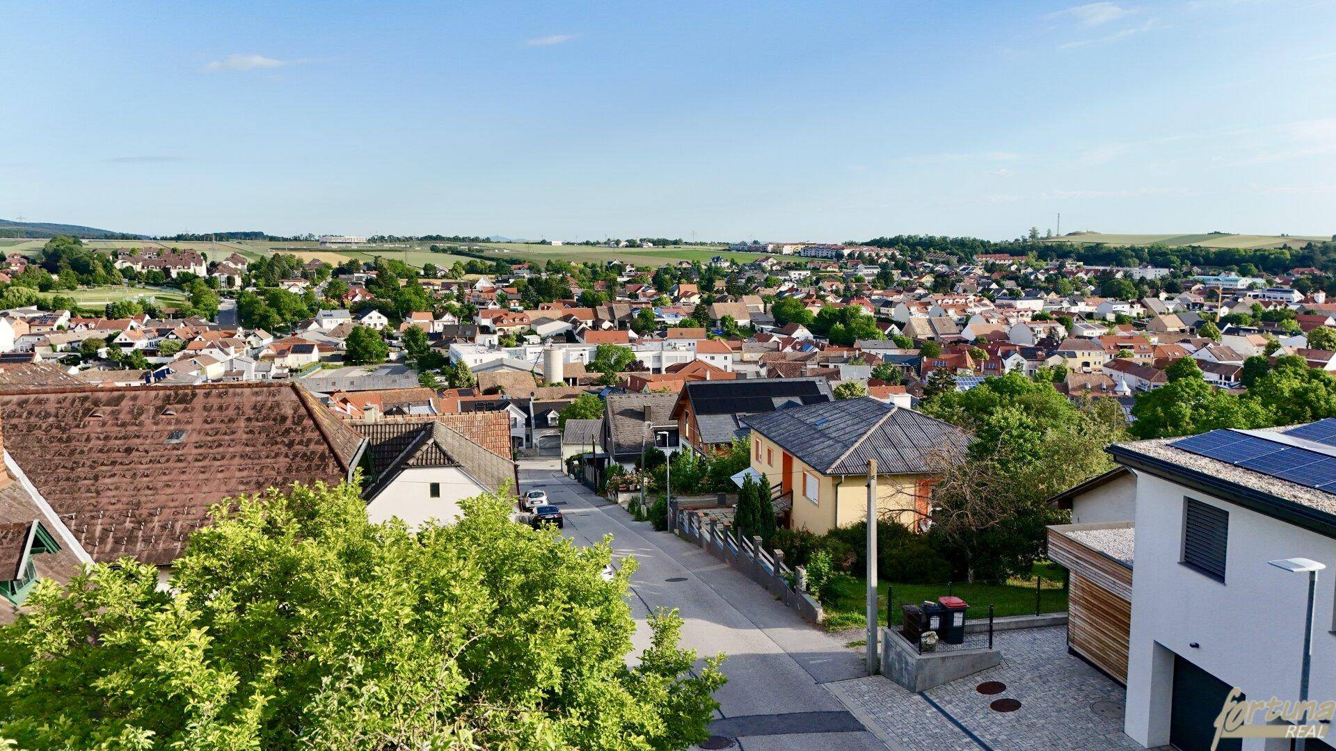 Weitblick über eine Wohnsiedlung mit Feldern und Hügeln am Horizont.