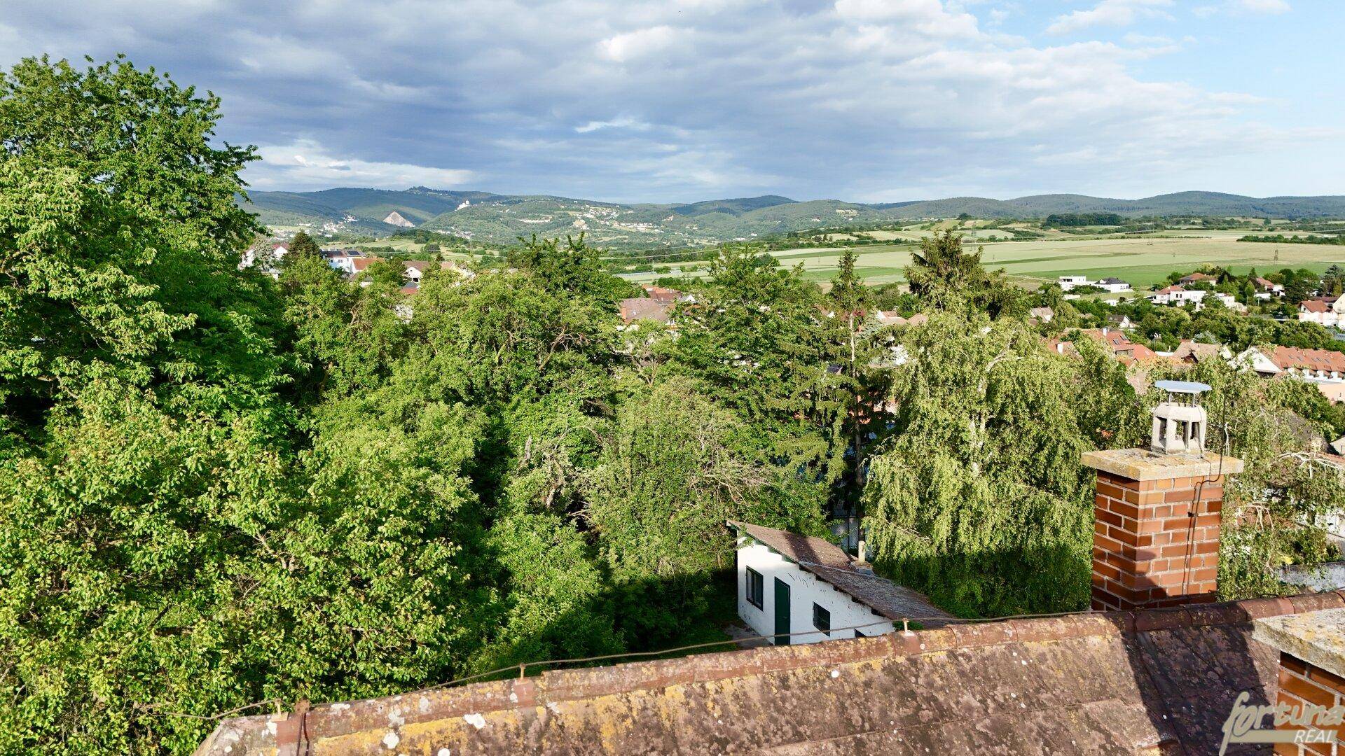 Panoramablick über bewaldete Hügel und eine ländliche Umgebung unter bewölktem Himmel.