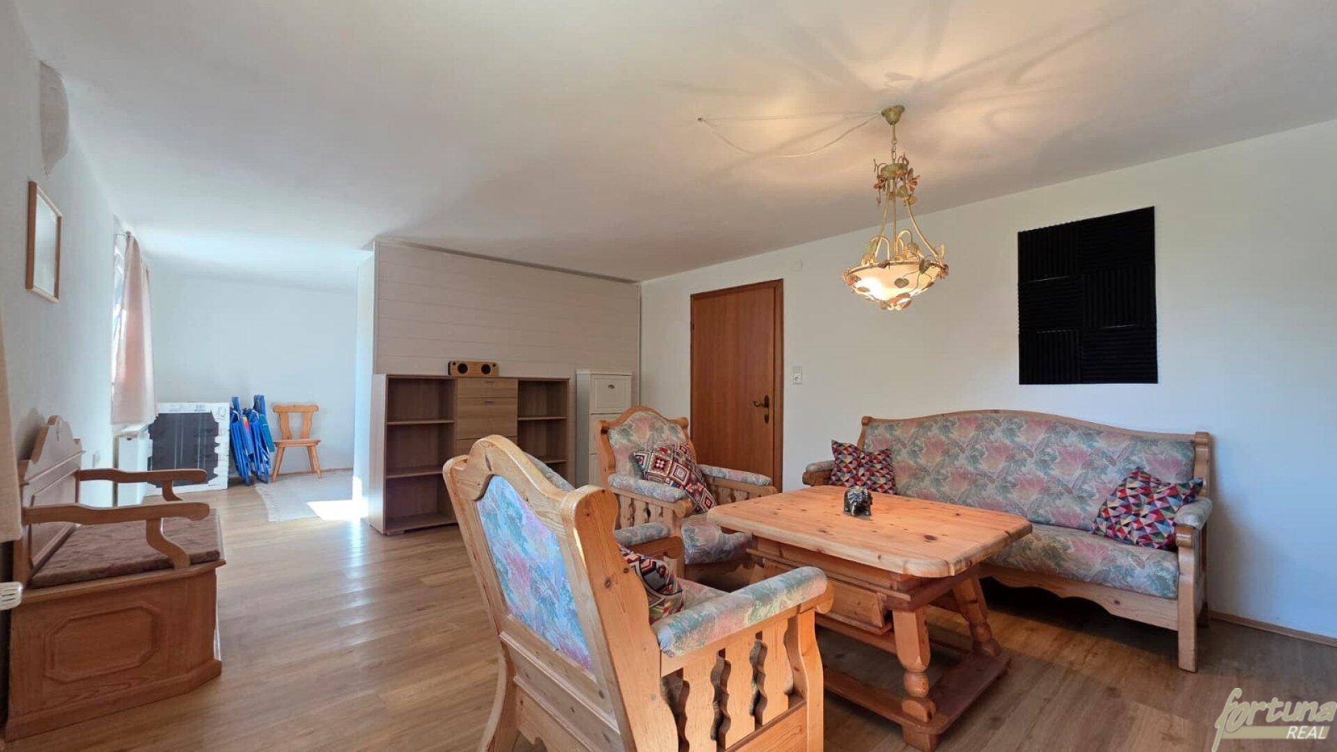 Geräumiges Wohnzimmer mit traditionellen Holzmöbeln, Holzboden und einem dekorativen Kronleuchter.