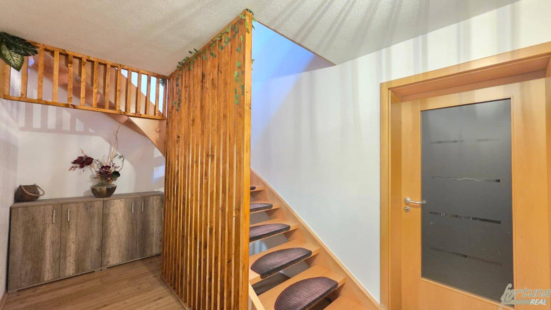Heller Eingangsbereich mit Holztreppe, dekorativer Holzvertäfelung und weiß gestrichenen Wänden.