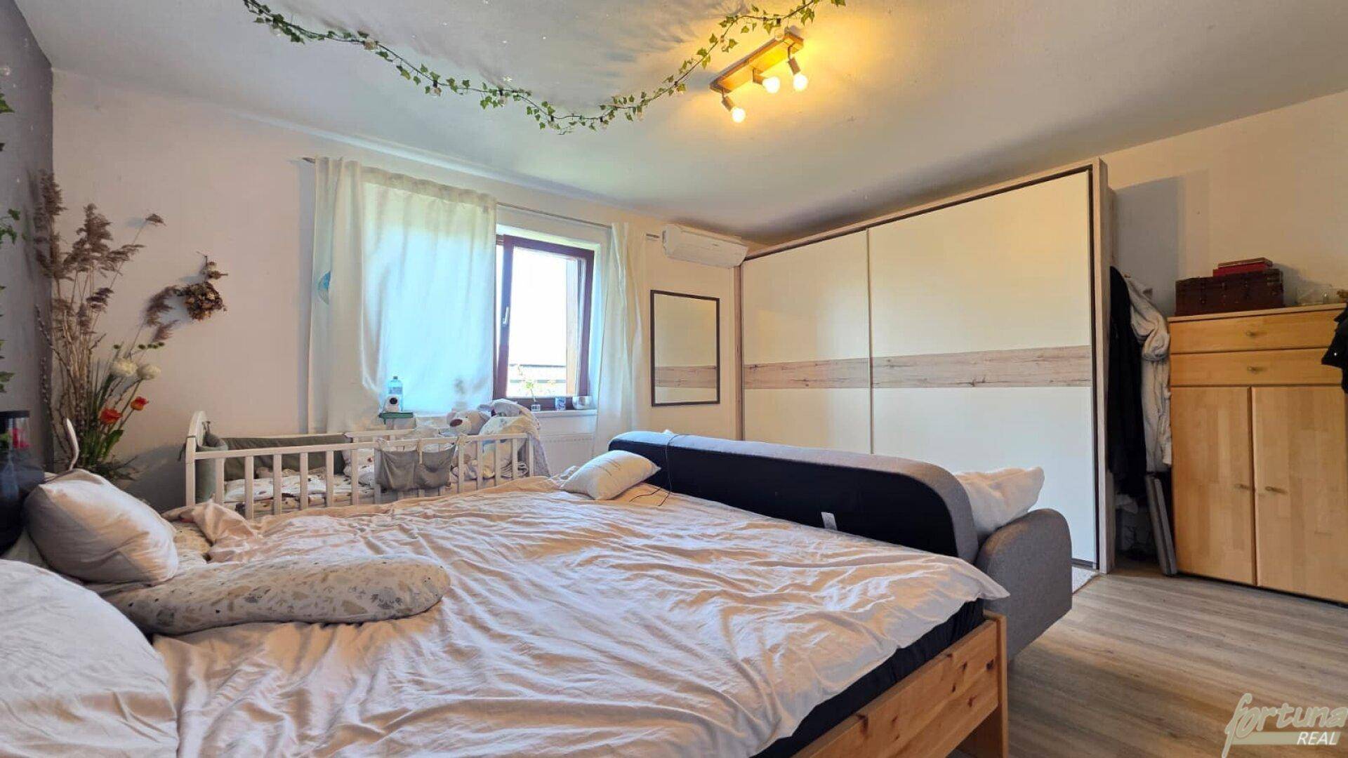 Schlafzimmer mit großem Bett, Babybett und einem geräumigen Kleiderschrank mit Schiebetüren.
