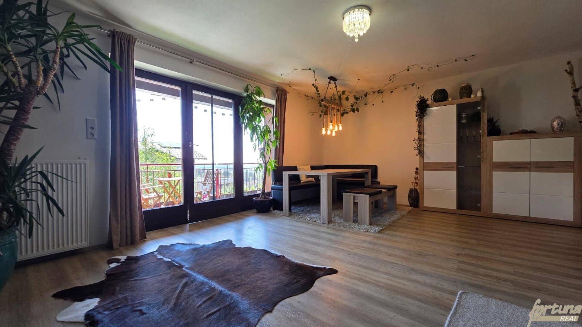 Essbereich mit Holztisch und Sitzbank, großen Fenstern und Zugang zu einem Balkon.