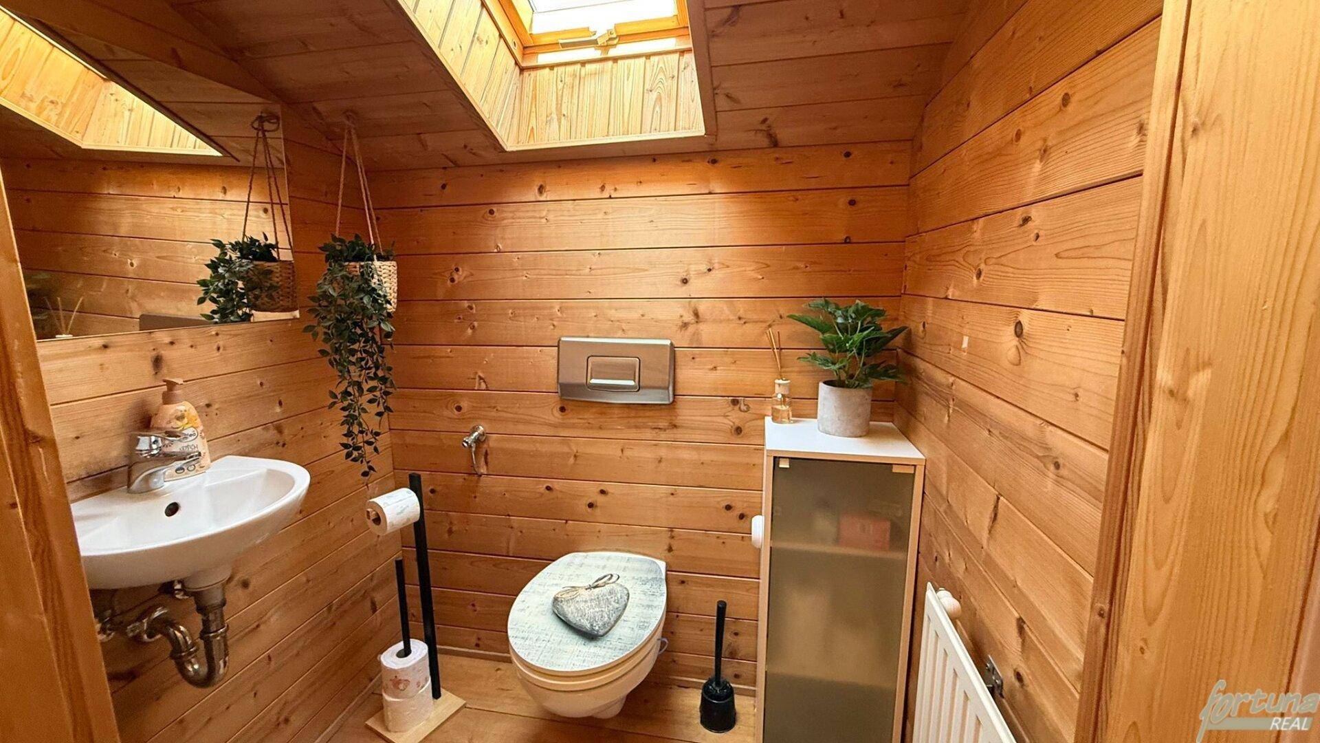 Gemütliches Gäste-WC mit Holzvertäfelung, Waschbecken, Toilette und einem Dachfenster für Tageslicht.