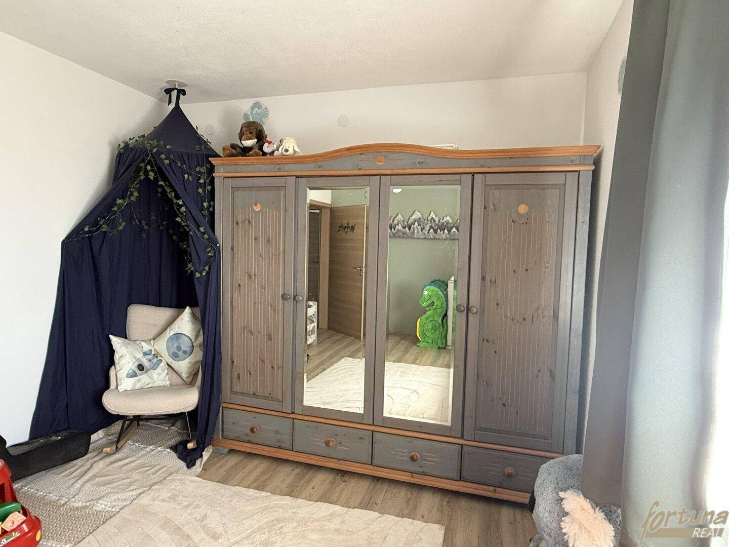 Kinderzimmer mit großem Holzschrank, Spiegeltüren und einem gemütlichen Himmelbettbereich.