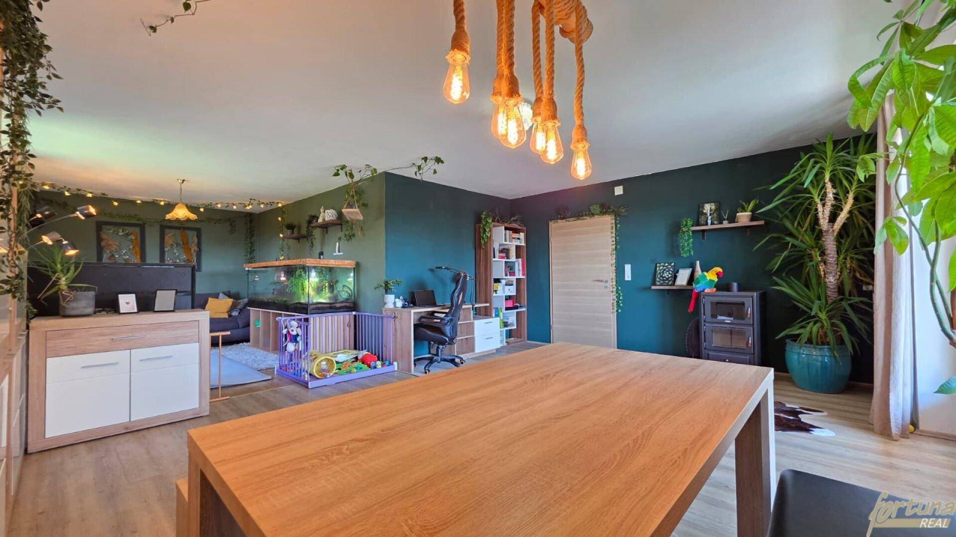 Offener Wohnbereich mit Essbereich, Arbeitsplatz und Aquarium, dekoriert mit Pflanzen und dunklen Wänden.
