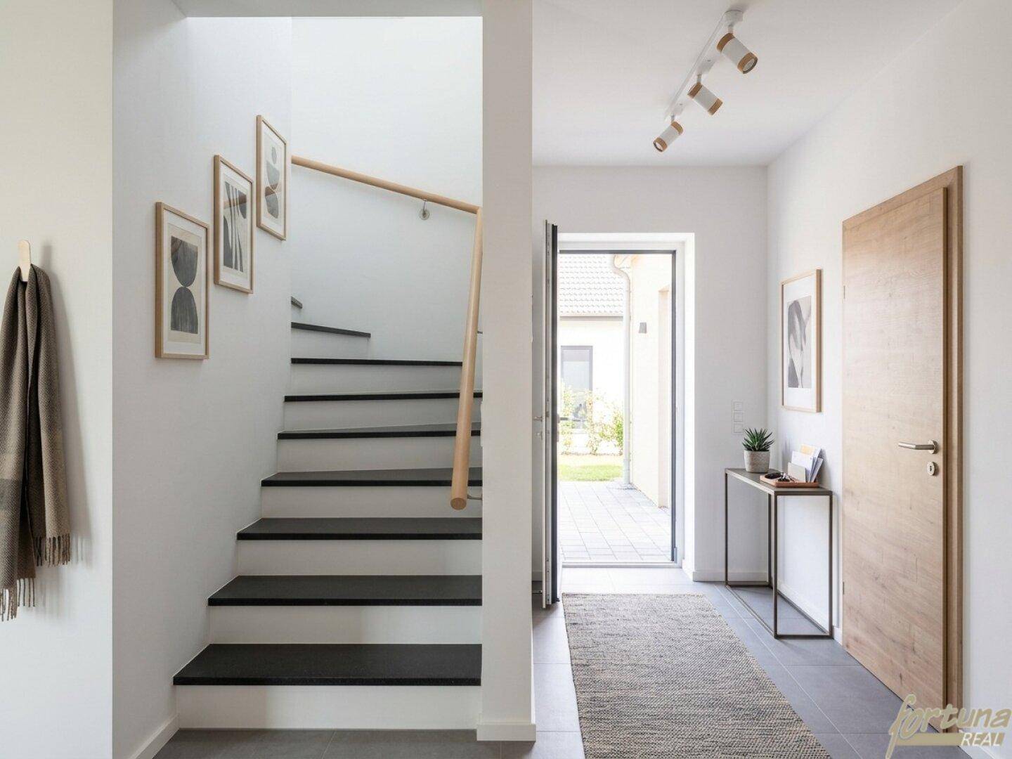 Moderner Eingangsbereich mit offener Treppe und Zugang zum gepflasterten Außenbereich.