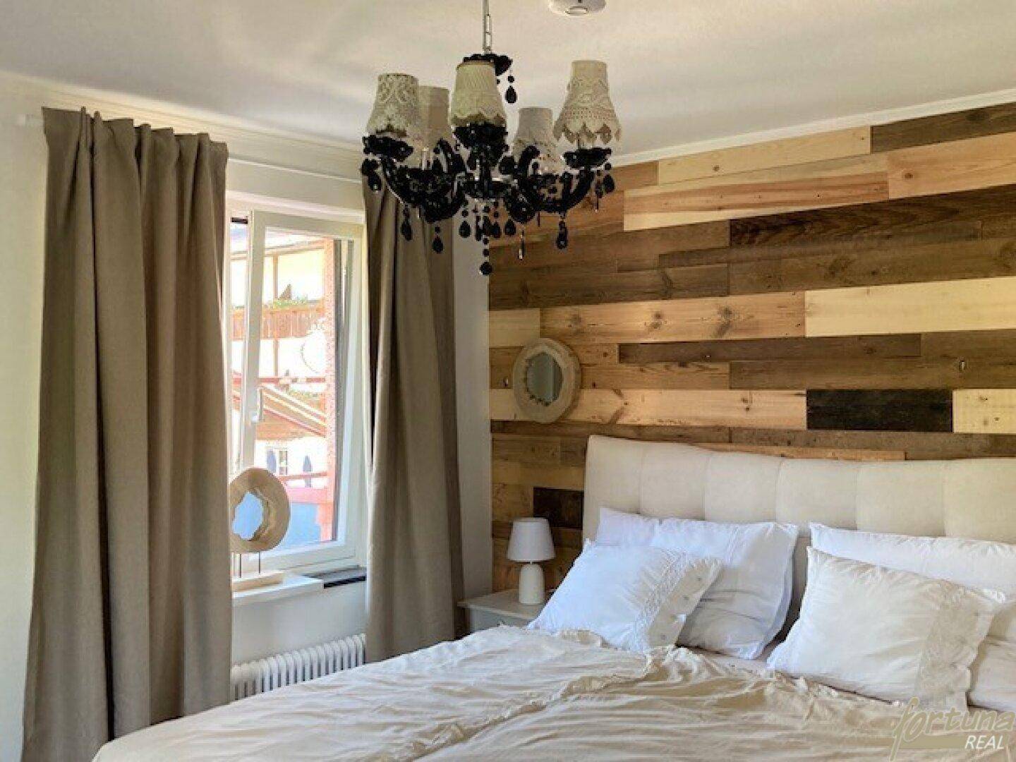 Gemütliches Schlafzimmer mit Holzwand, großem Bett und einem dekorativen Kronleuchter.