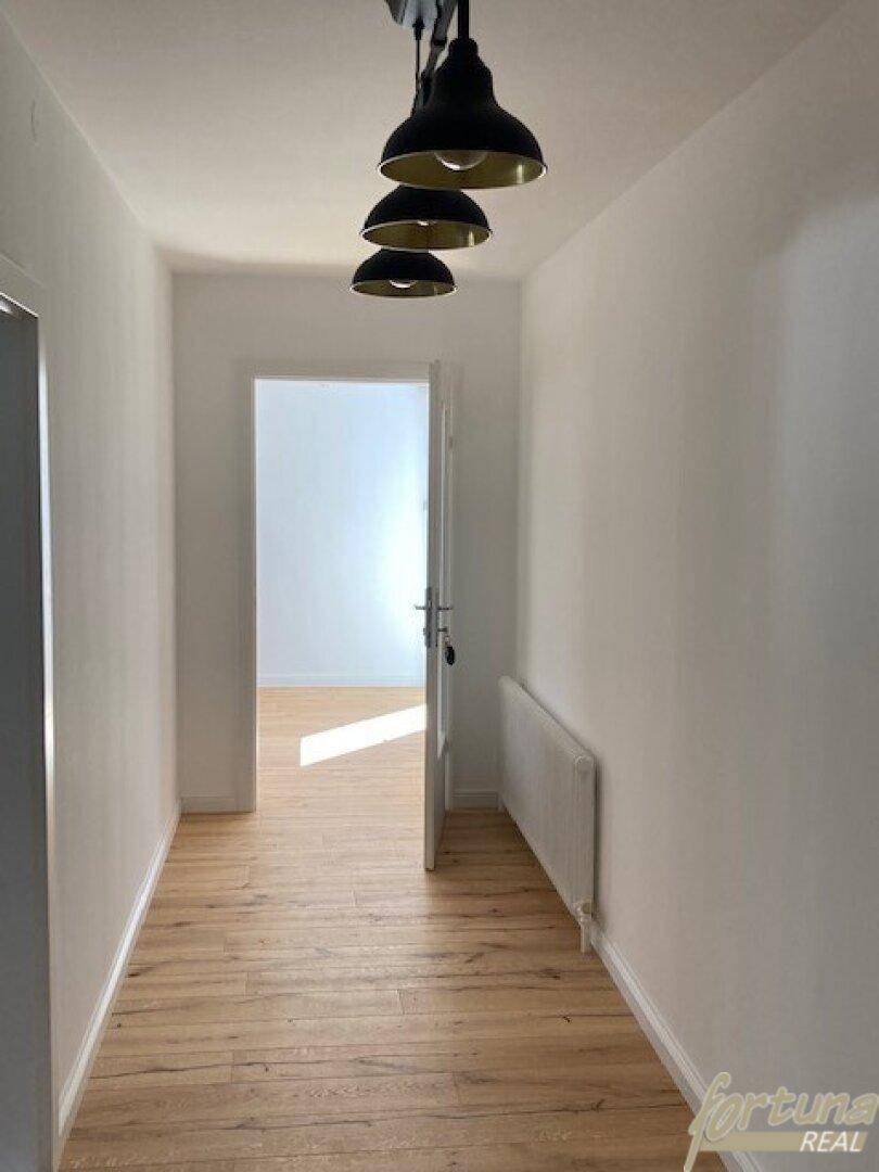 Heller Flur mit hellem Holzfußboden, weißen Wänden und modernen Hängelampen.
