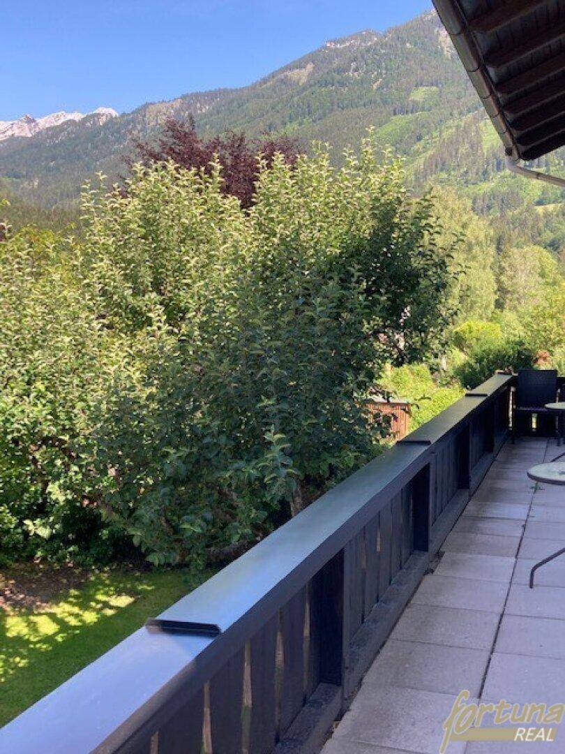Balkon mit Sitzgelegenheiten und weitem Blick auf den grünen Garten und die umliegenden Berge.