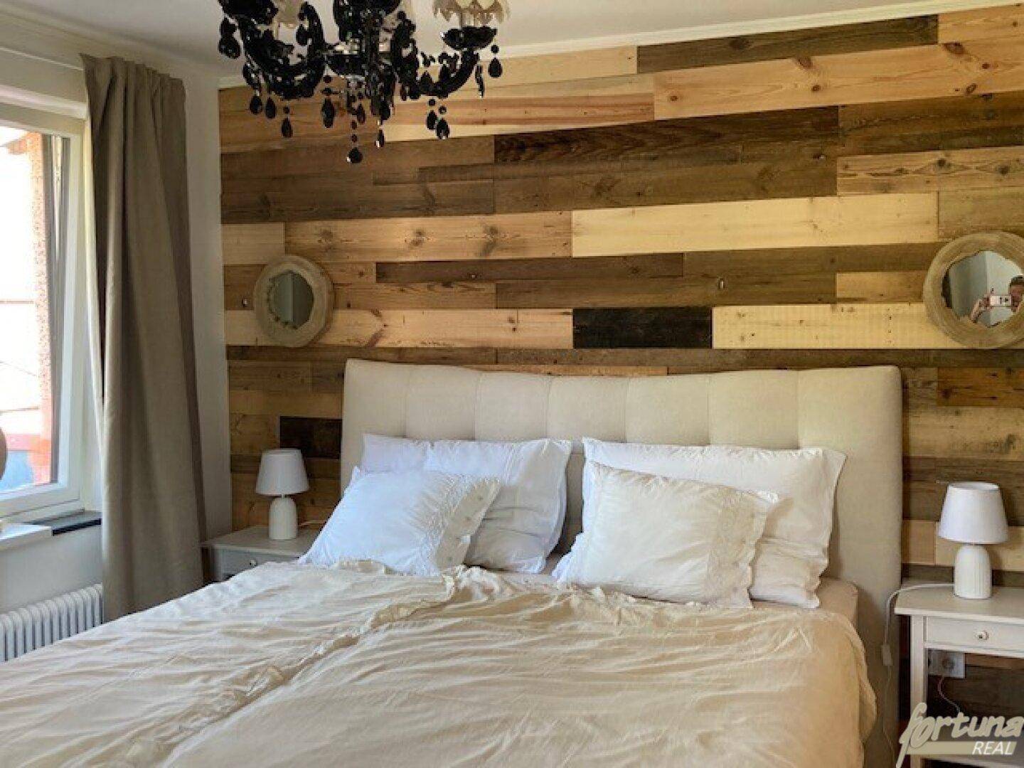 Schlafzimmer mit Holzakzentwand, bequemen Bett und stilvollem Kronleuchter.