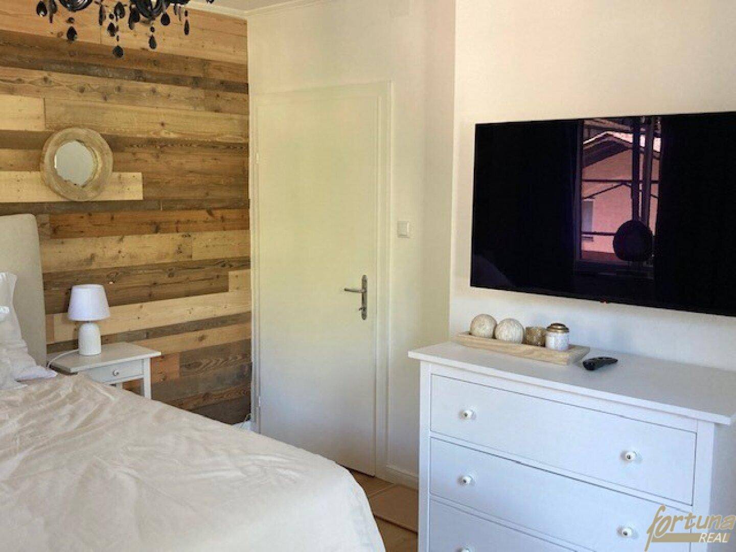 Schlafzimmerbereich mit Kommode, Wandfernseher und einer Holzakzentwand.